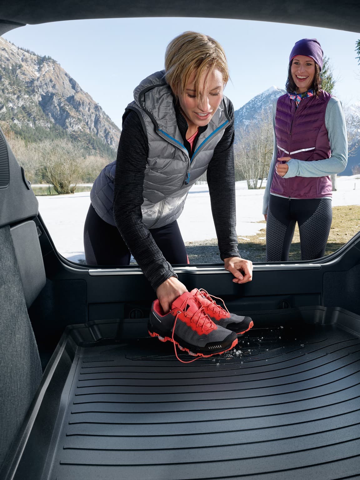 Two women next to each other, one is putting her shoes in the trunk