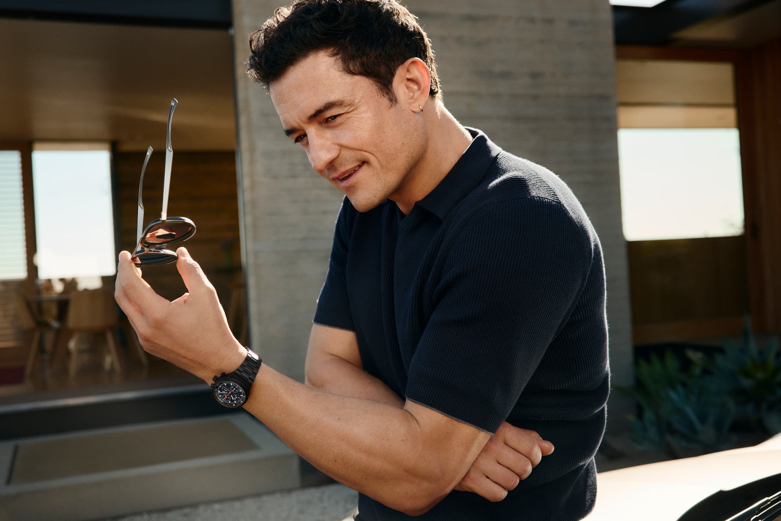 Orlando Bloom weaing the Chronograph 1 - All Black Numbered Edition on his wrist, standin in front of a house, smiling