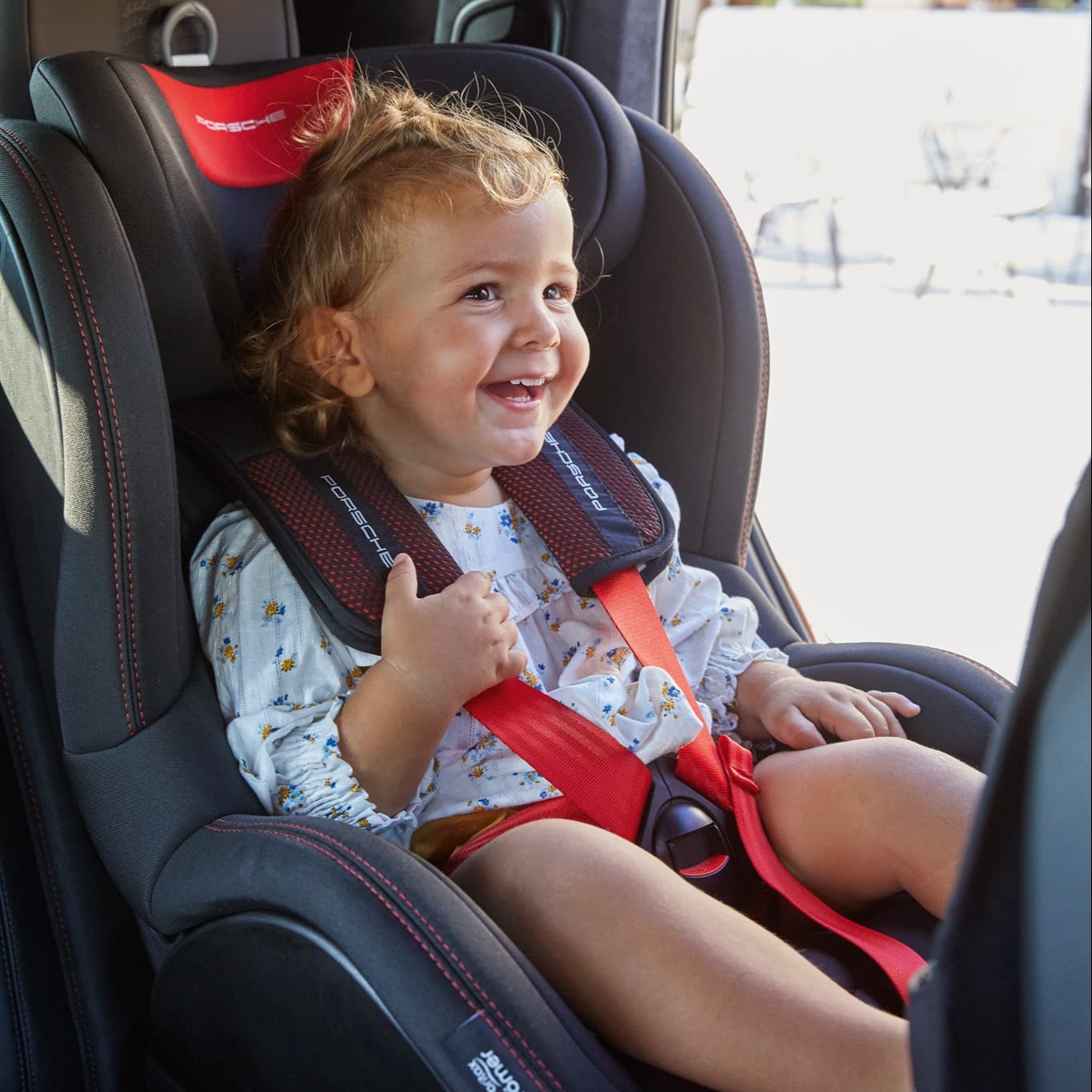 A little girl sitting in a Porsche child seat