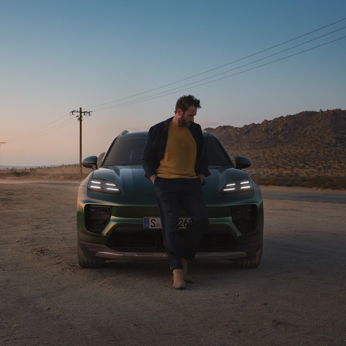 A man is standing in front of a darkgreen Porsche Macan next to a road