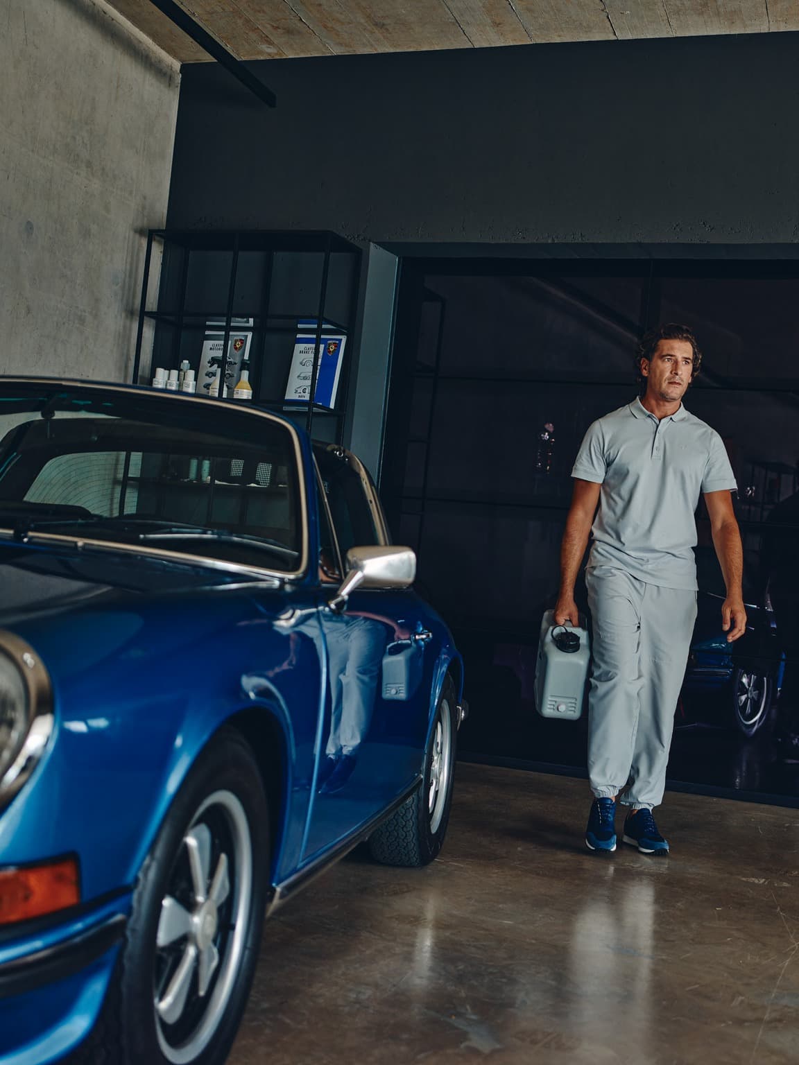 Man is walking through a garage next to a blue Porsche classic car