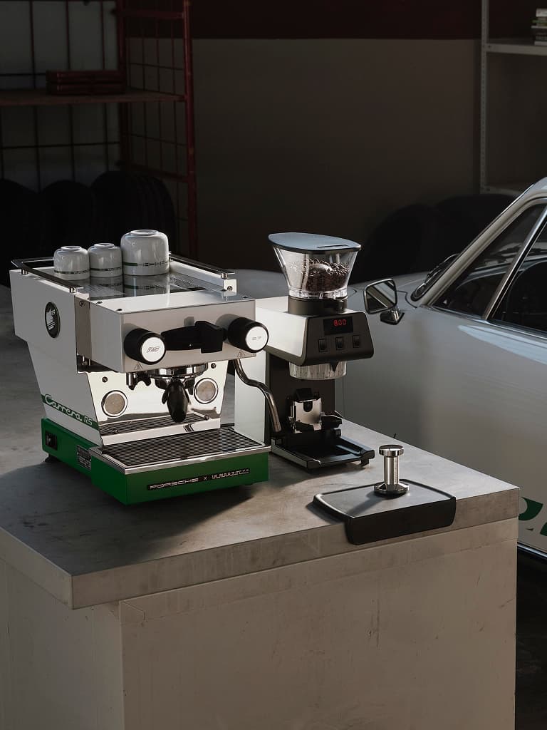 Macchina da caffè La Marzocco in argento con design Carrera RS 2.7 accanto a un’auto originale Carrera RS 2.7