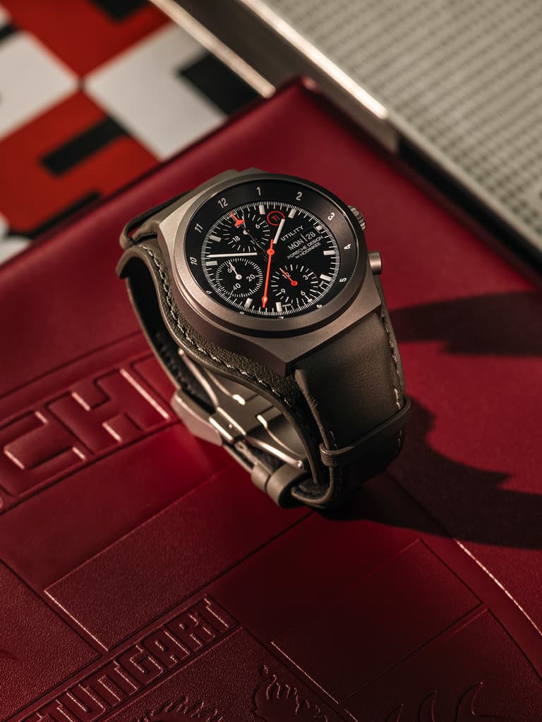 Orologio da polso cronografo con quadrante nero e cinturino in pelle nera, su superficie rossa con sfondo a motivo da corsa.