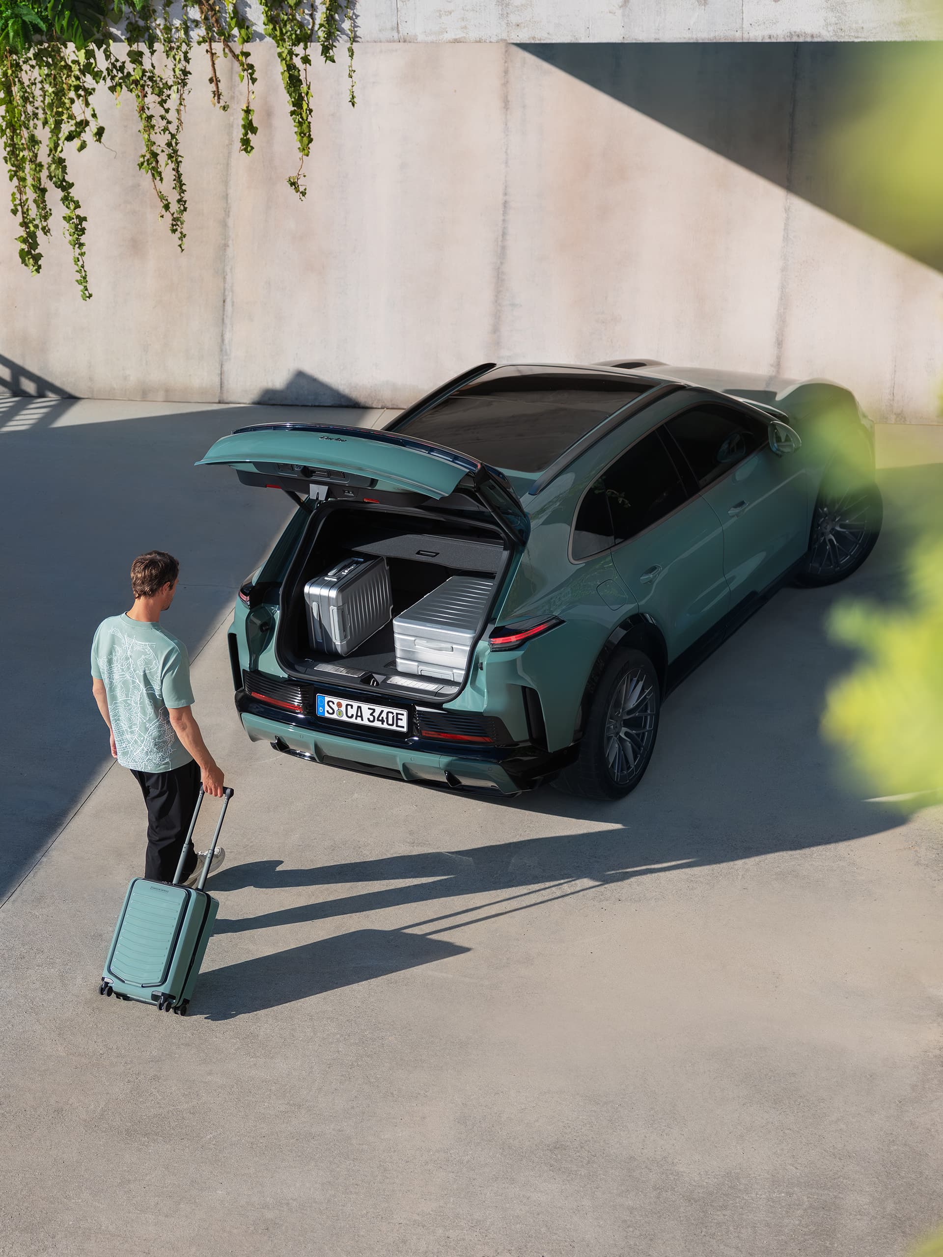 Man med turkos resväska står vid den öppna bagageluckan på en grön Porsche, bagage i lastutrymmet