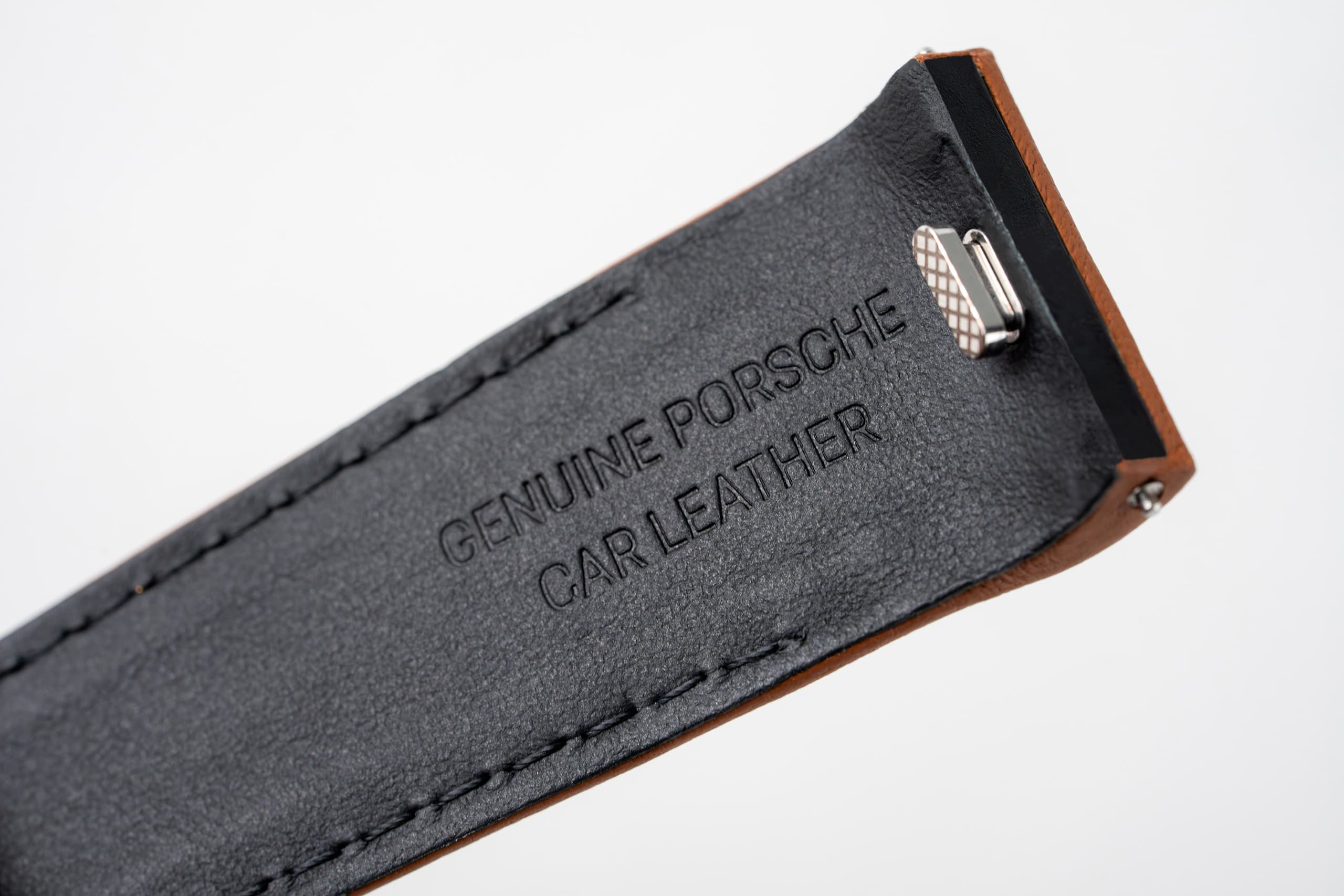 Gros plan sur une lanière en cuir noir embossée « Genuine Porsche Car Leather » avec un clip métallique.