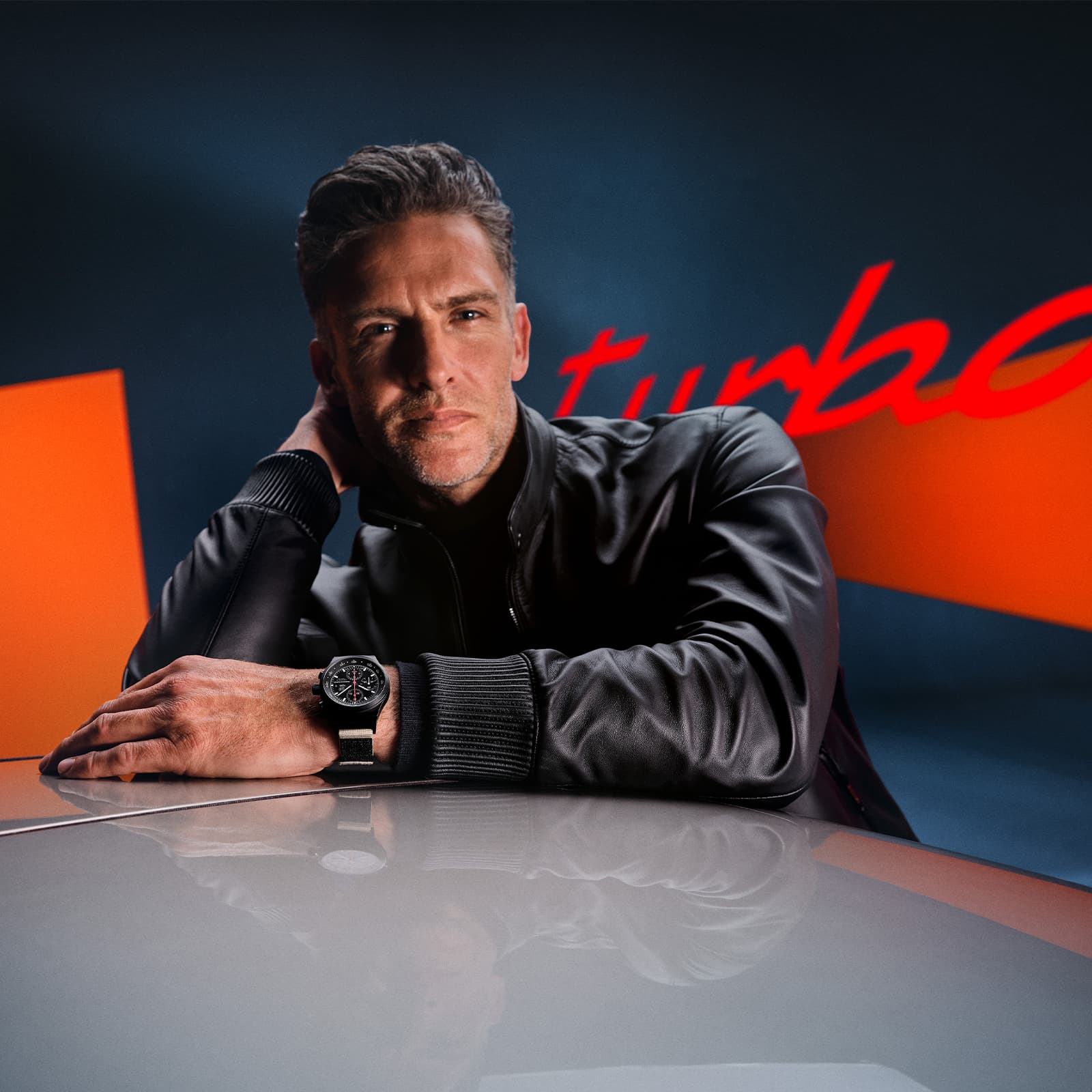 Man is leaning on a car roof with lettering turbo in the background