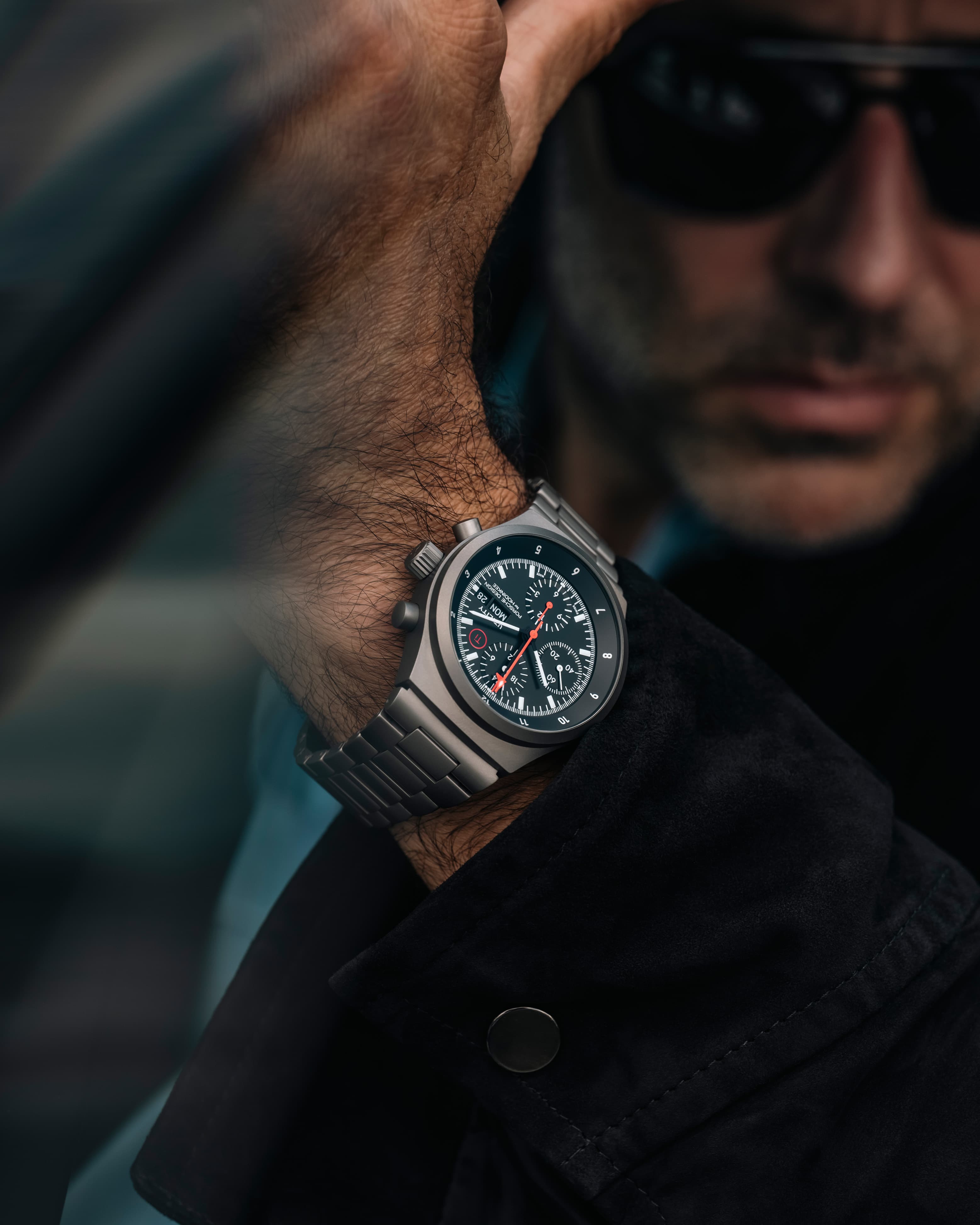 Primo piano di un uomo che indossa un orologio cronografo nero con lancette rosse e bracciale in metallo.