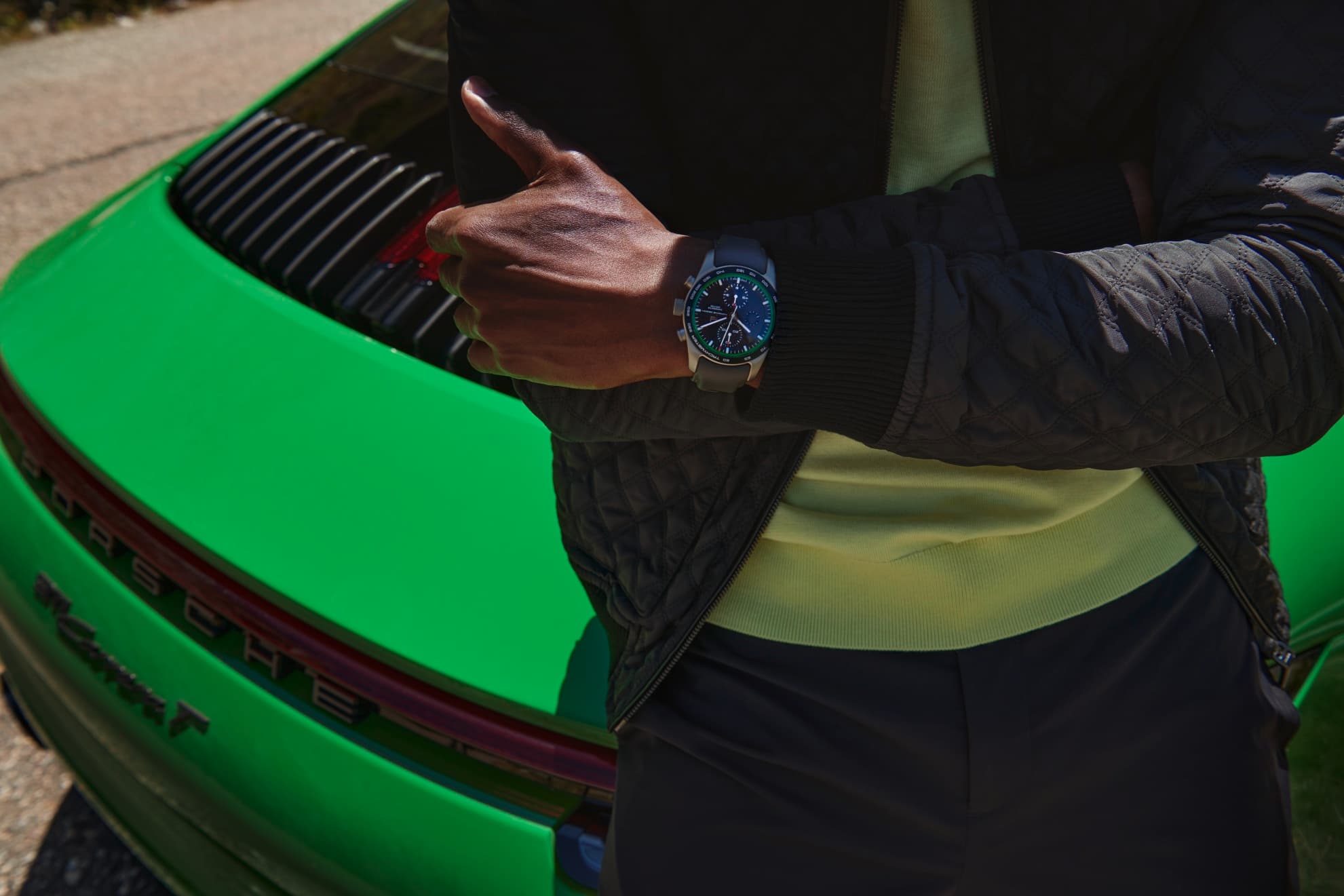Man wearing a color matching Porsche Design custim-build Chonograph on his wrist, leaning on a green Porsche 911