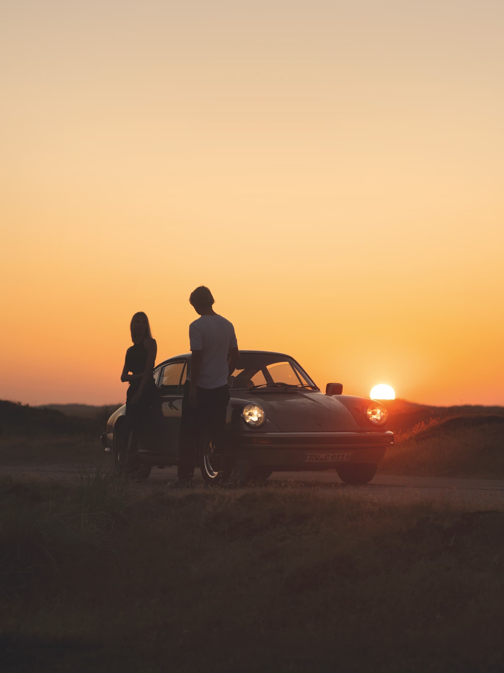 Two people at sunset standing in front of a classic 911