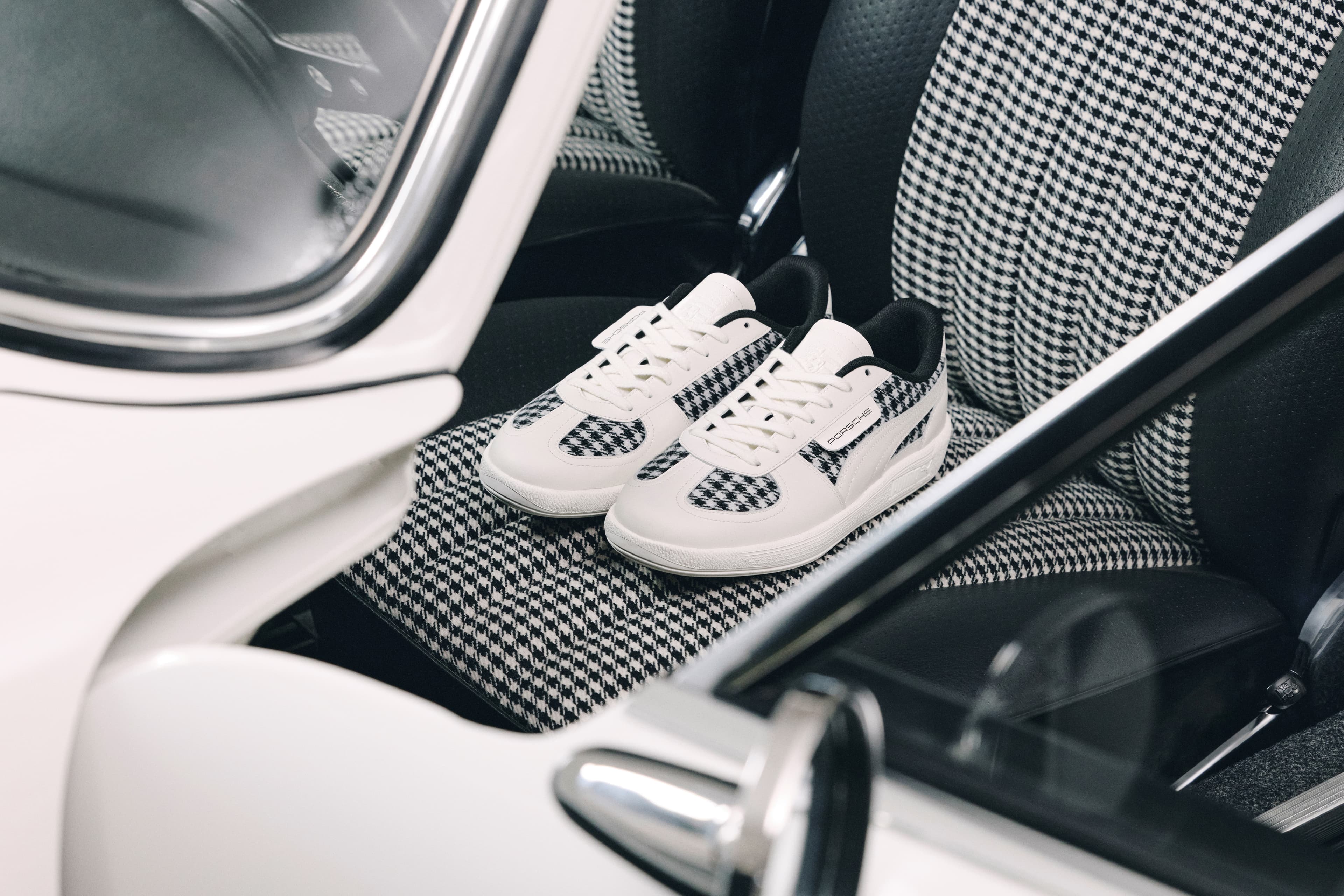 Black-and-white Porsche sneakers with houndstooth pattern on a houndstooth car seat in the interior.