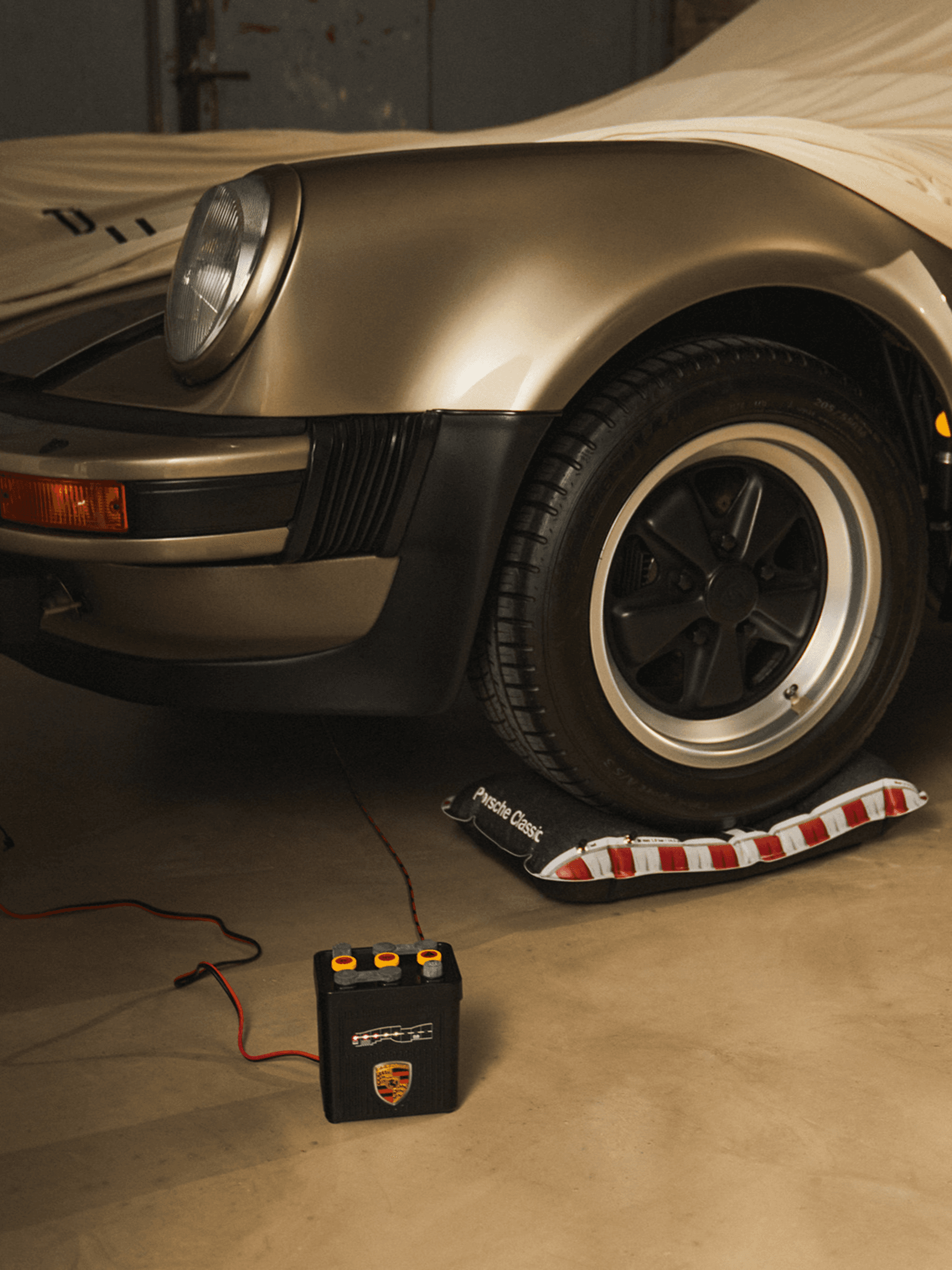 Classic Porsche front with gold finish, black wheel, and battery charger on garage floor.