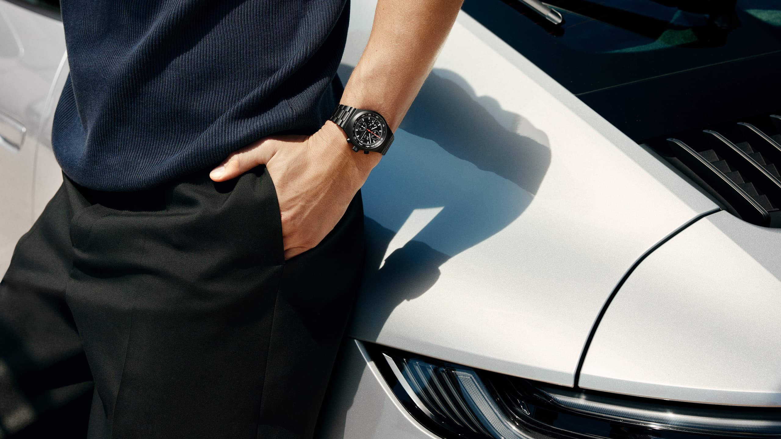 Man leaning against white Porsche door, wearing a Chronograph 1 - All Black Numbered Edition on his wrist