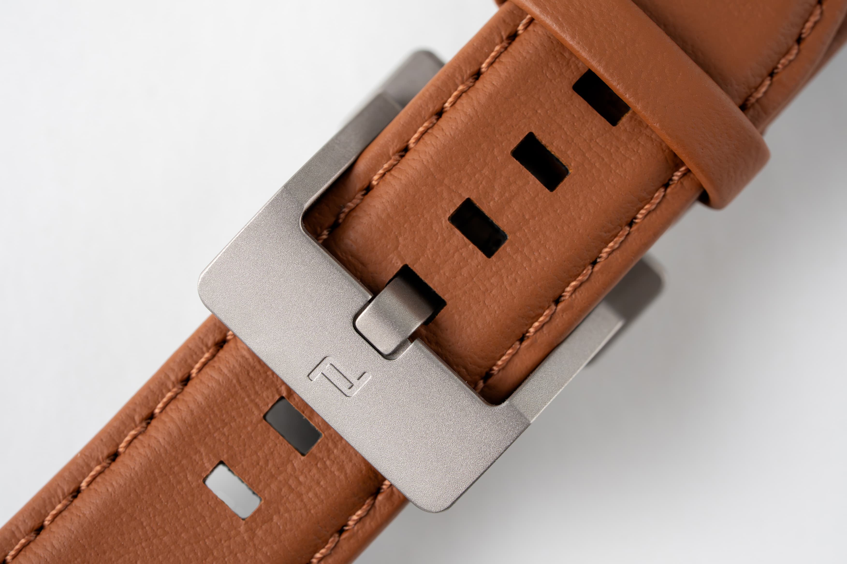 Close-up of a brown leather strap with rectangular cutouts and a silver metal buckle.
