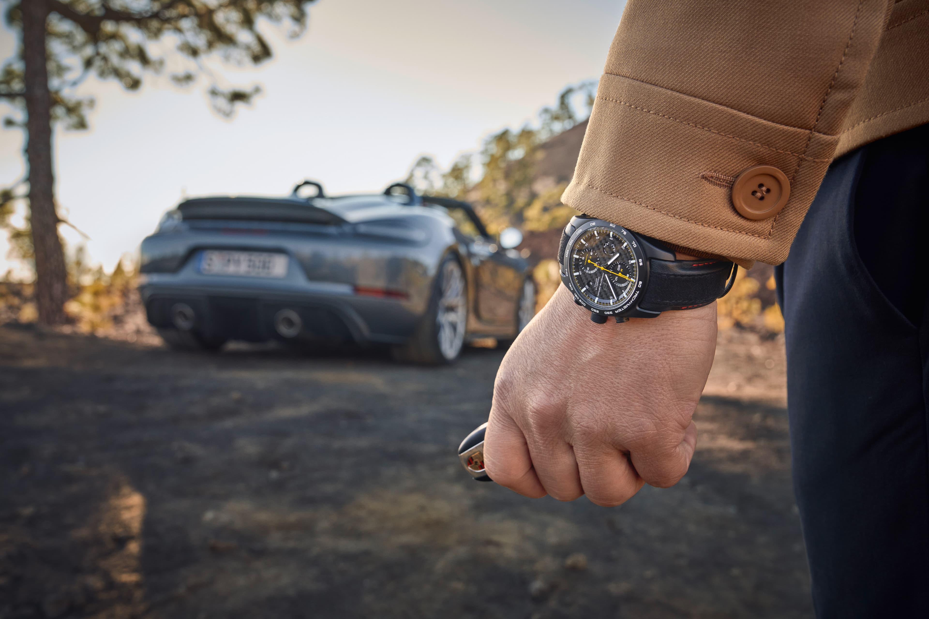 Pictured is a man wearing the Porsche Chronograph 718 Spyder RS from behind and in the background is a blue Porsche 718 Spyder