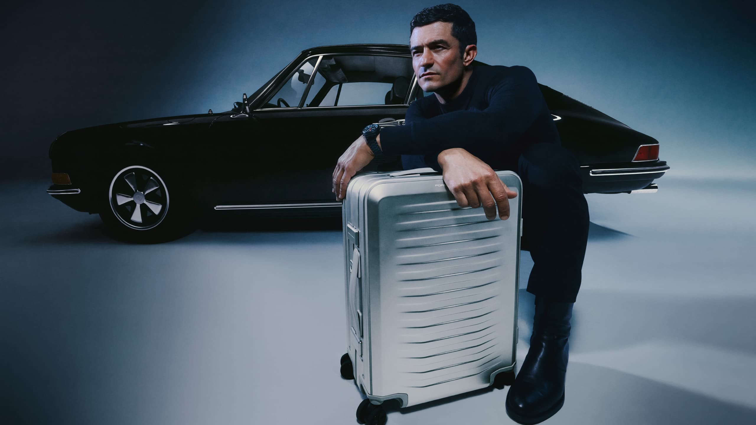 Orlando Bloom with Porsche Design Roaster Aluminum Trolley, Porsche car in background