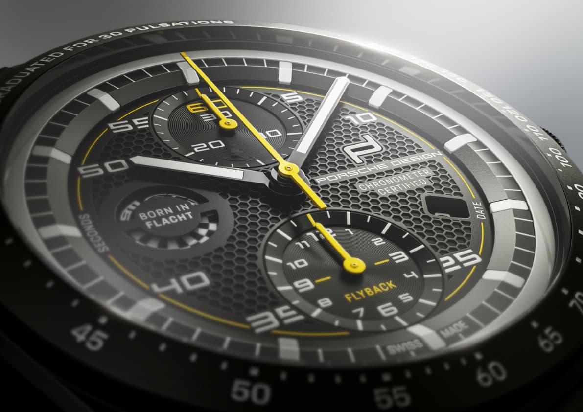 Close-up of a Porsche Design chronograph with a black honeycomb dial, yellow hands, and white hour markers.