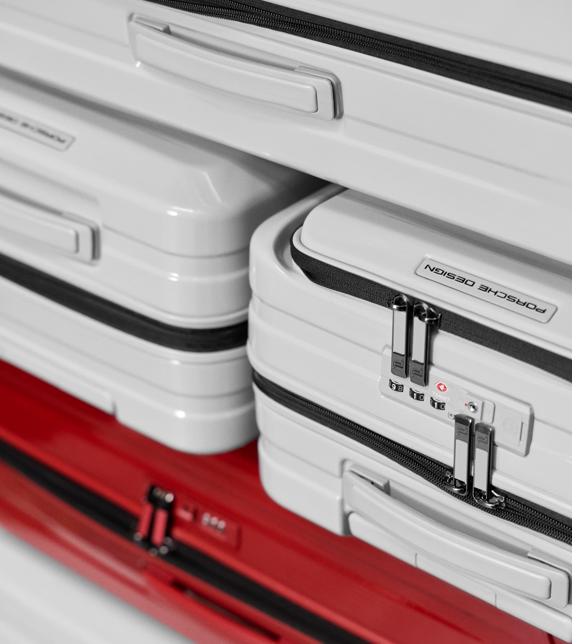 Close-up of white Porsche Design hard-shell suitcase with black zipper and TSA lock, stacked on red luggage.