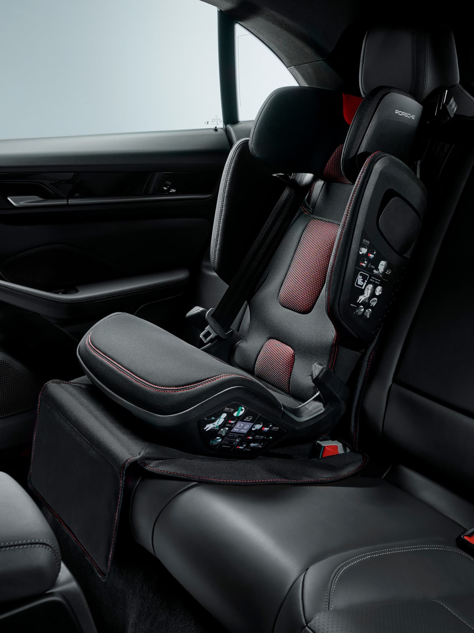 Black and red Porsche child seat in a car's rear seat, featuring adjustable headrest and safety harness.