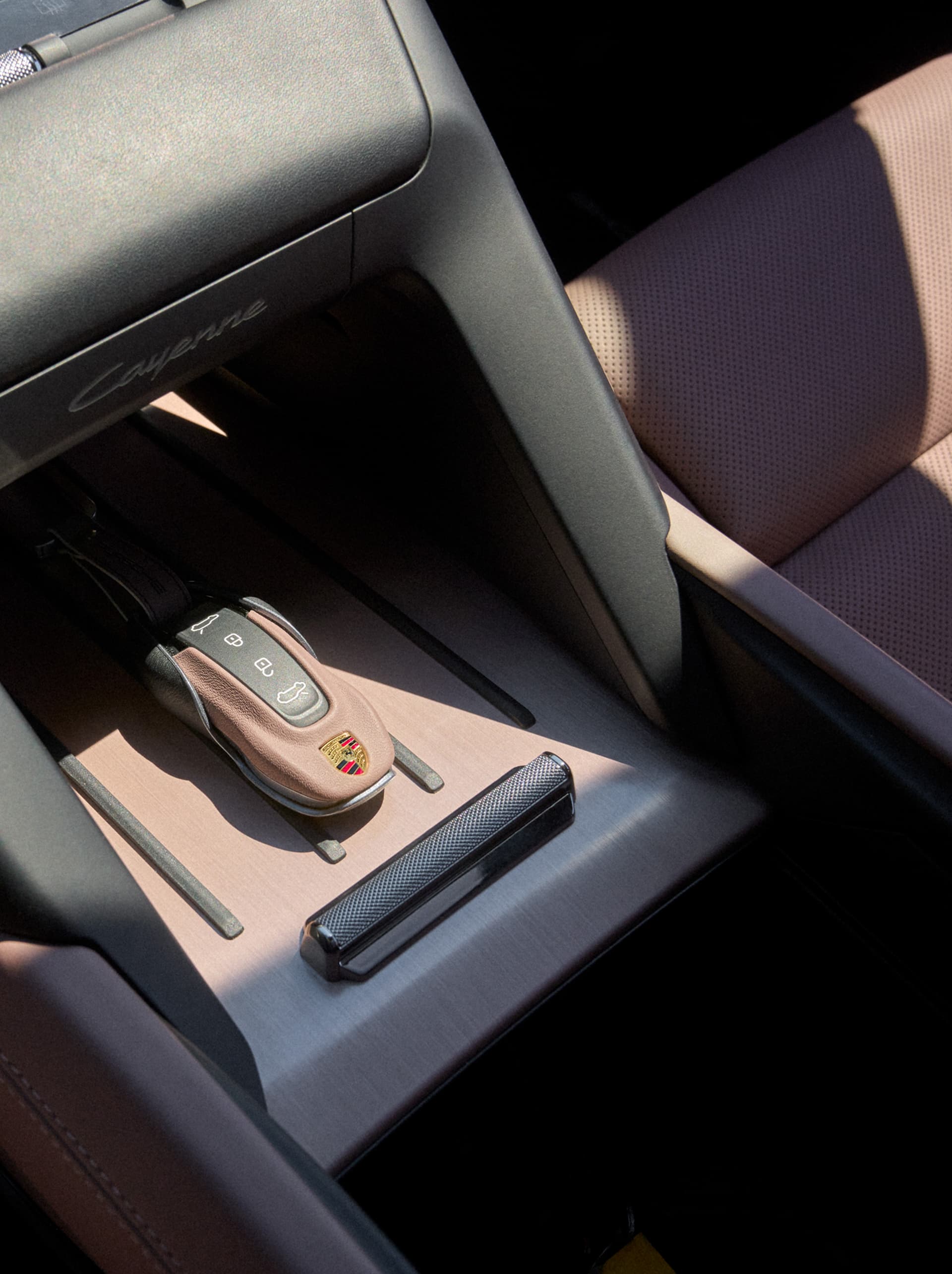 Interno auto Porsche con portachiavi in pelle marrone su console centrale in metallo spazzolato, accanto a sedile in pelle traforata