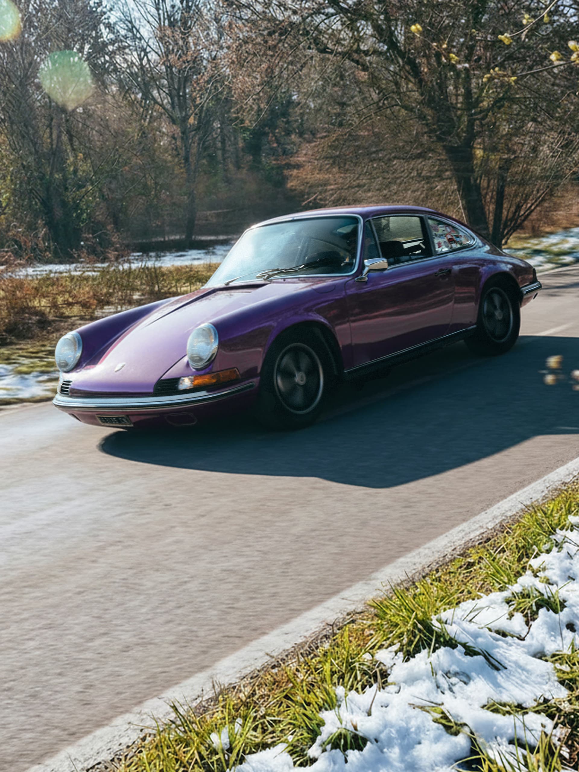 Lila Vintage-Porsche fährt auf einer sonnigen Straße, umgeben von Bäumen und Schneeflecken.