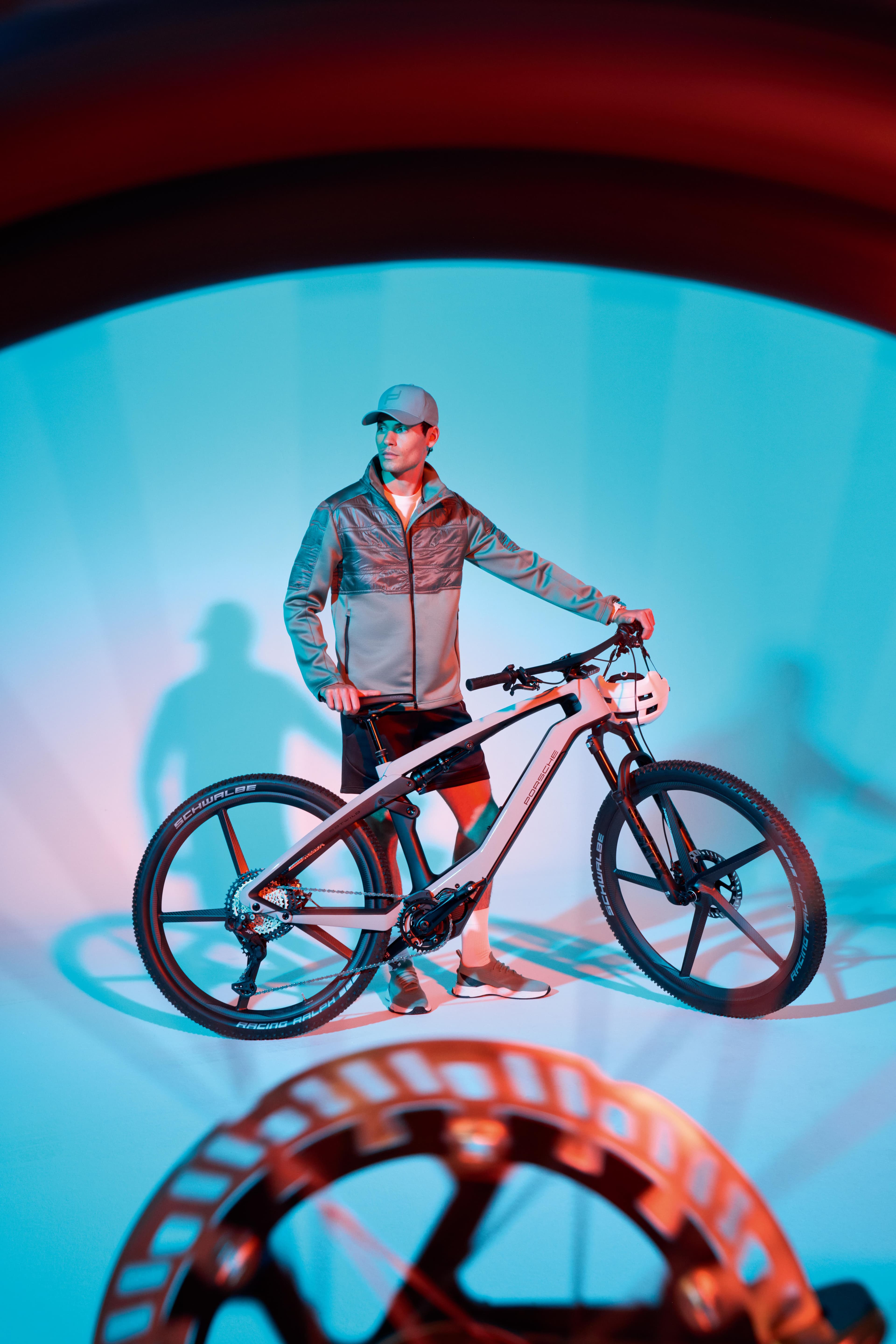 Homme en Porsche Design Sportsewear et Porsche eBike Sport photographié à travers un rayon de roue