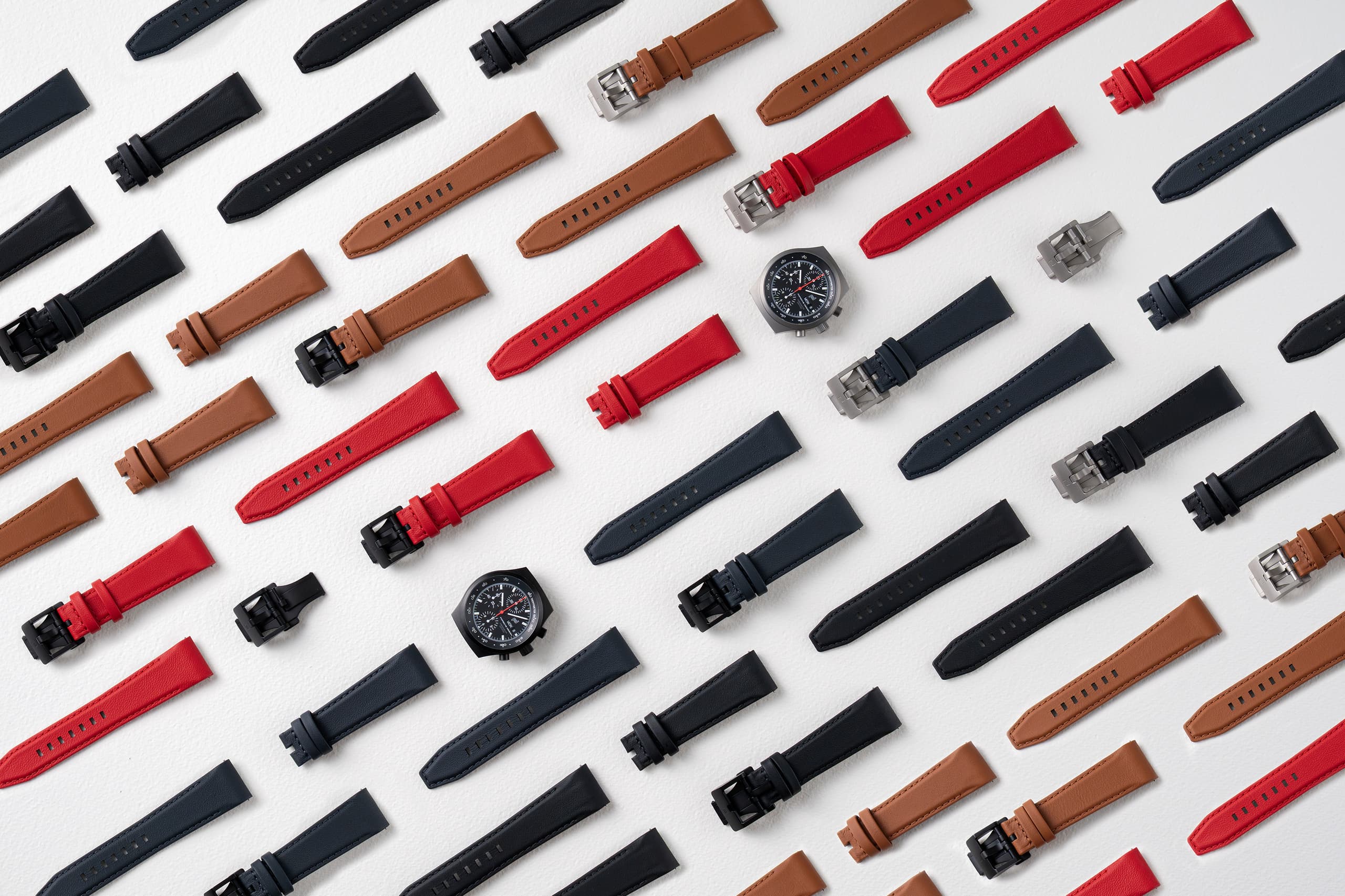 Verschiedene Uhrenarmbänder in Schwarz, Braun und Rot auf weißem Hintergrund, mit zwei Chronographen-Uhren.