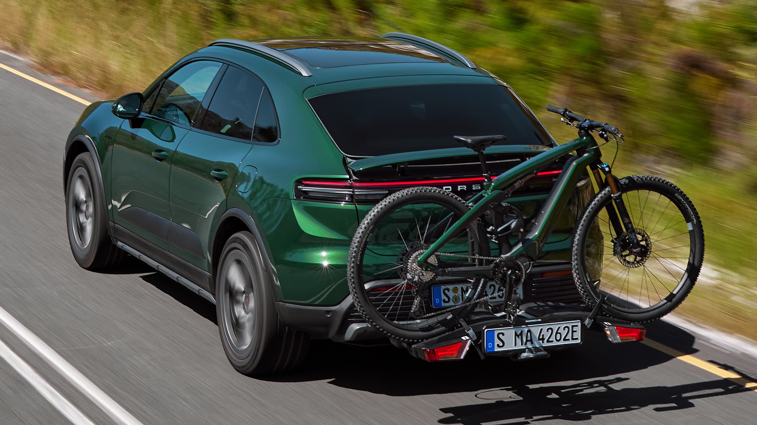 Porsche Macan w kolorze Oak Green na łonie natury, z rowerem Porsche eBike na bagażniku dachowym