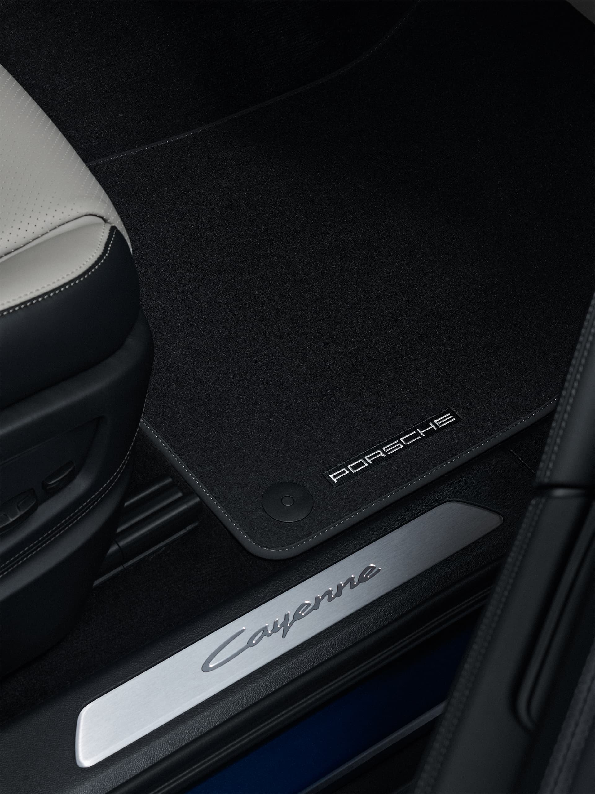 Fekete Porsche padlószőnyeg egy Cayenne-ben, a „Cayenne” küszöbdíszléc mellett hímzett PORSCHE felirattal.