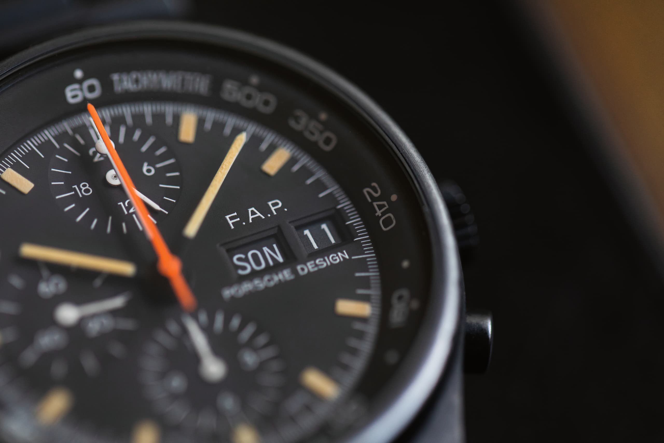 Zbliżenie na czarny chronograf Porsche Design z pomarańczową wskazówką sekundową i datownikiem.