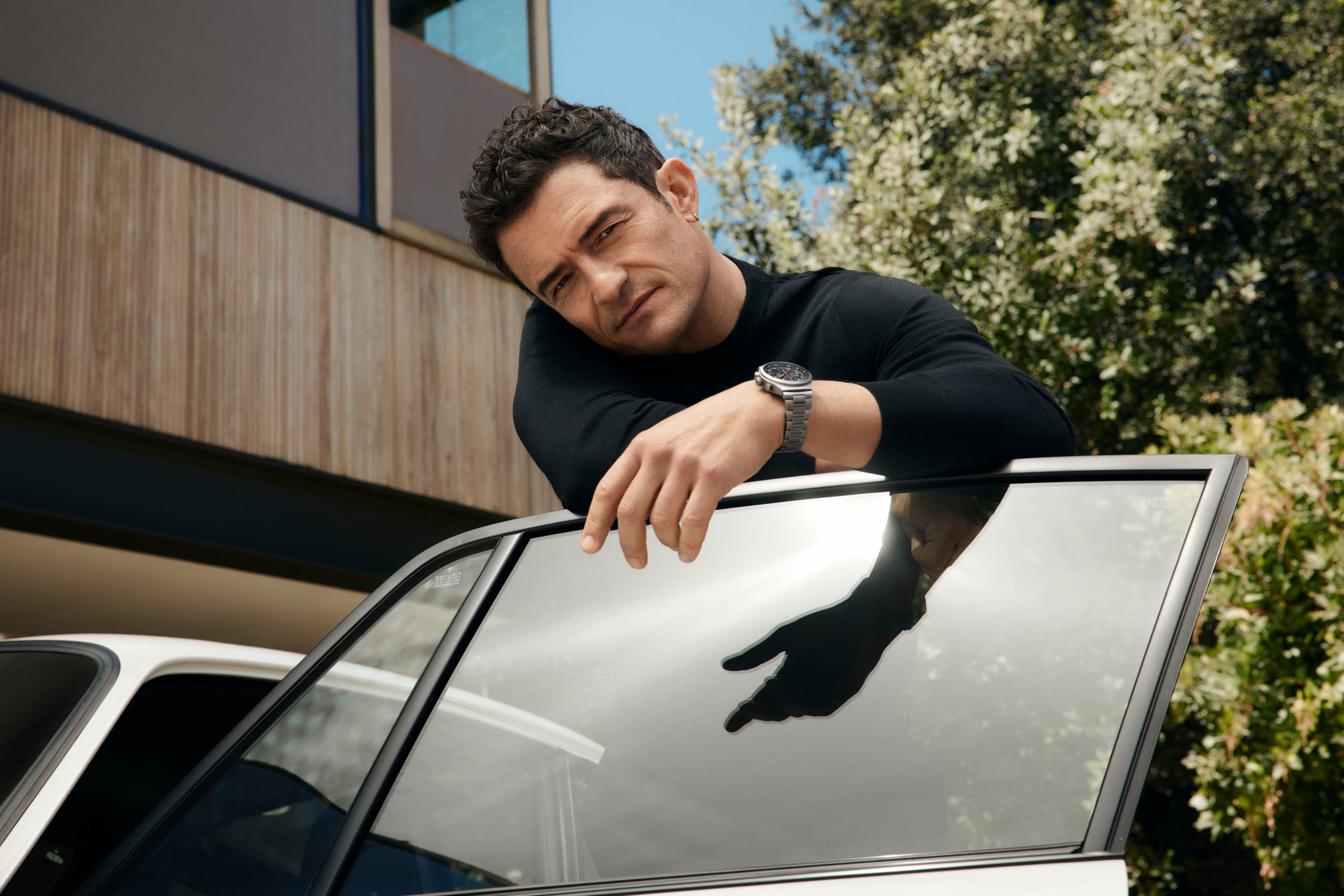 Orlando Bloom wears the Chronograph 1 - 1975 Limited Edition on his wrist and looks over the open door of a Porsche 911.