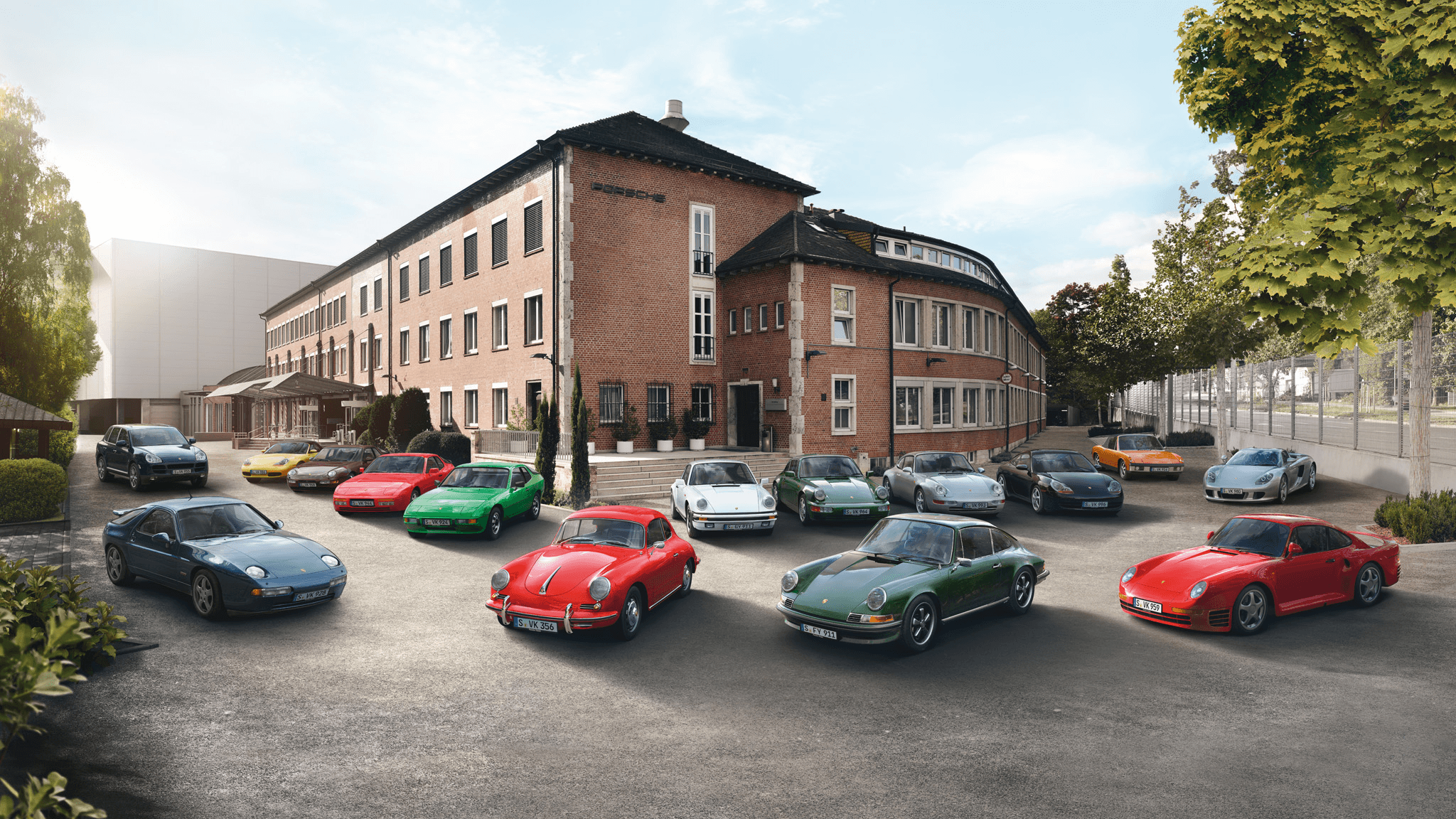 Various Porsche 911 models in a courtyard in front of a large building