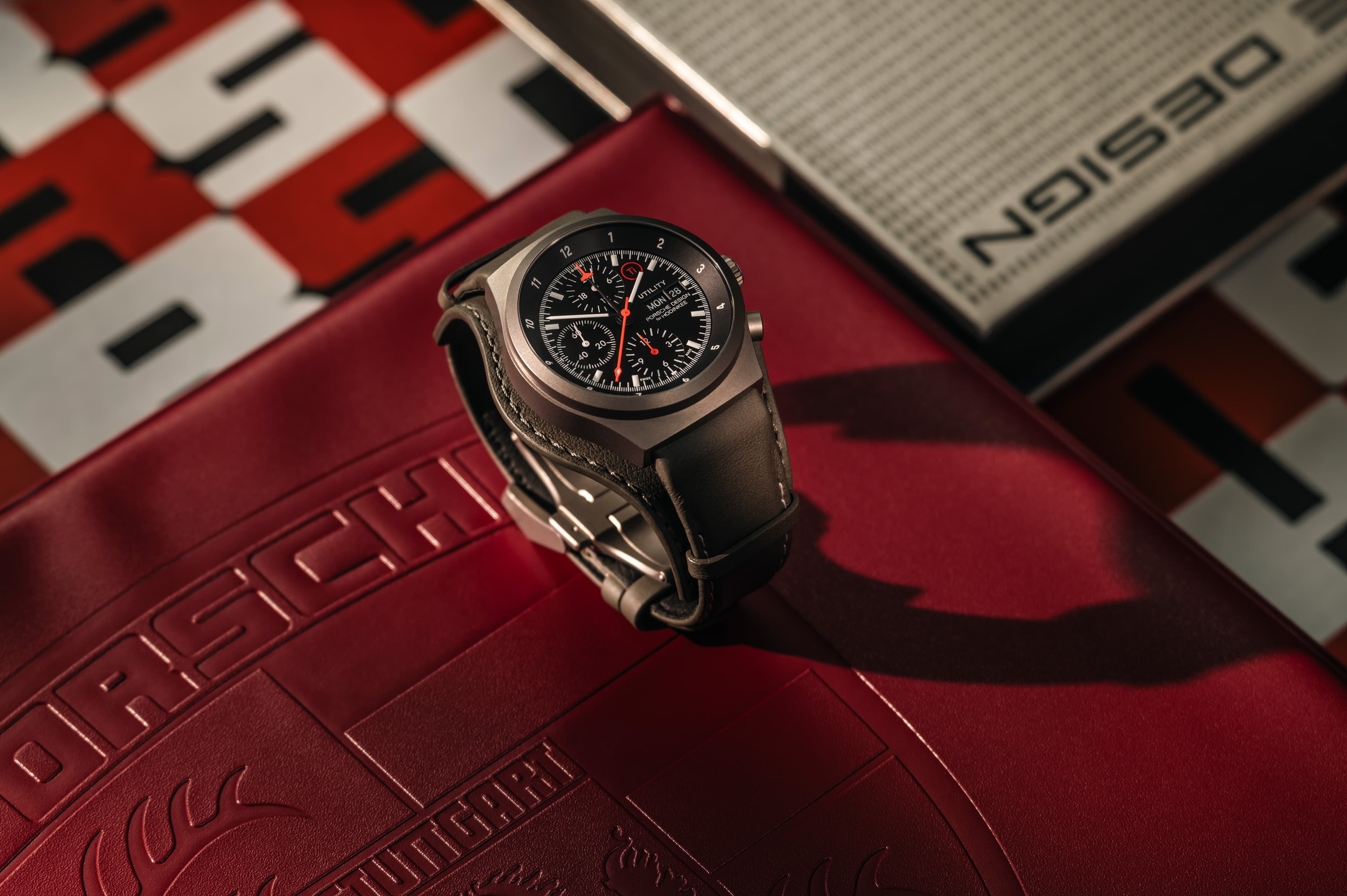 Cronografo da polso Porsche Design Chronograph 1 Utility nero, edizione Hodinkee, con cinturino in pelle, su sfondo rosso con design Porsche 911.