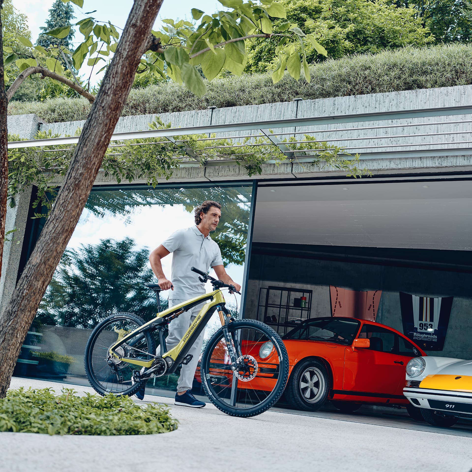 Man pushes his Porsche eBike in front of his garage with two historic Porsche 911s