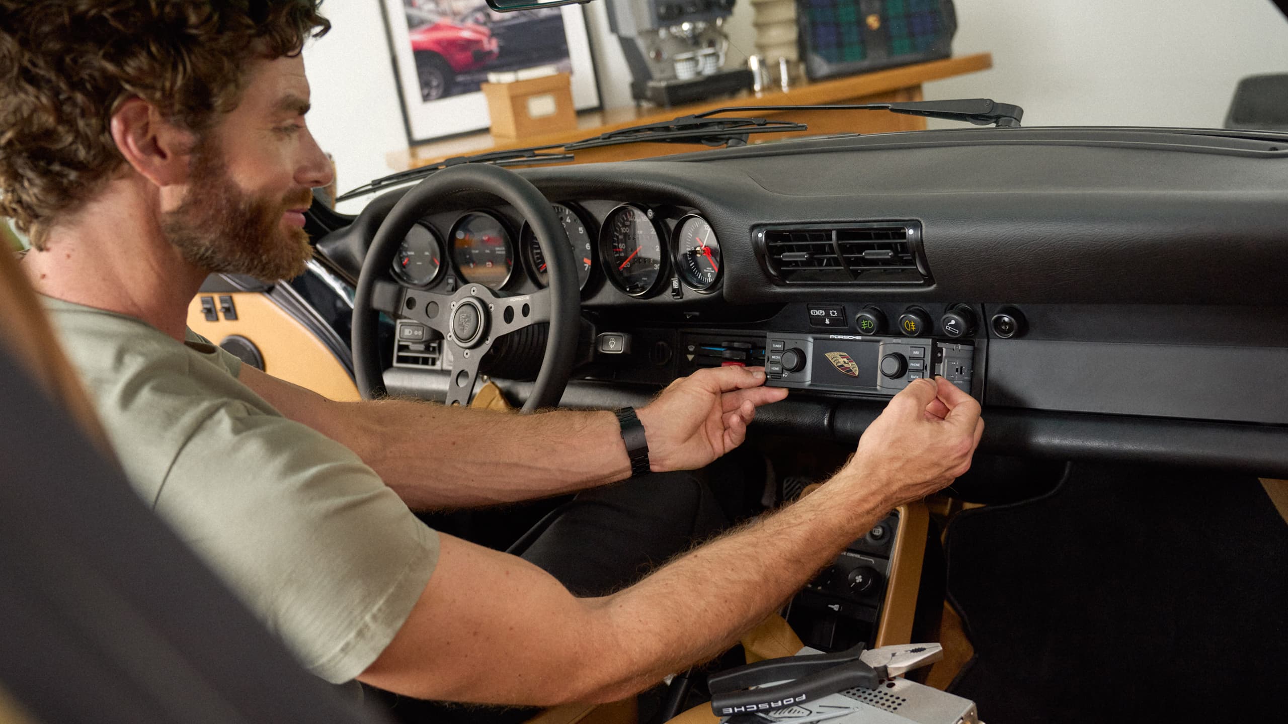 Homme installant une radio Porsche Classic sur le tableau de bord noir d’une Porsche 911, intérieur noir et beige.