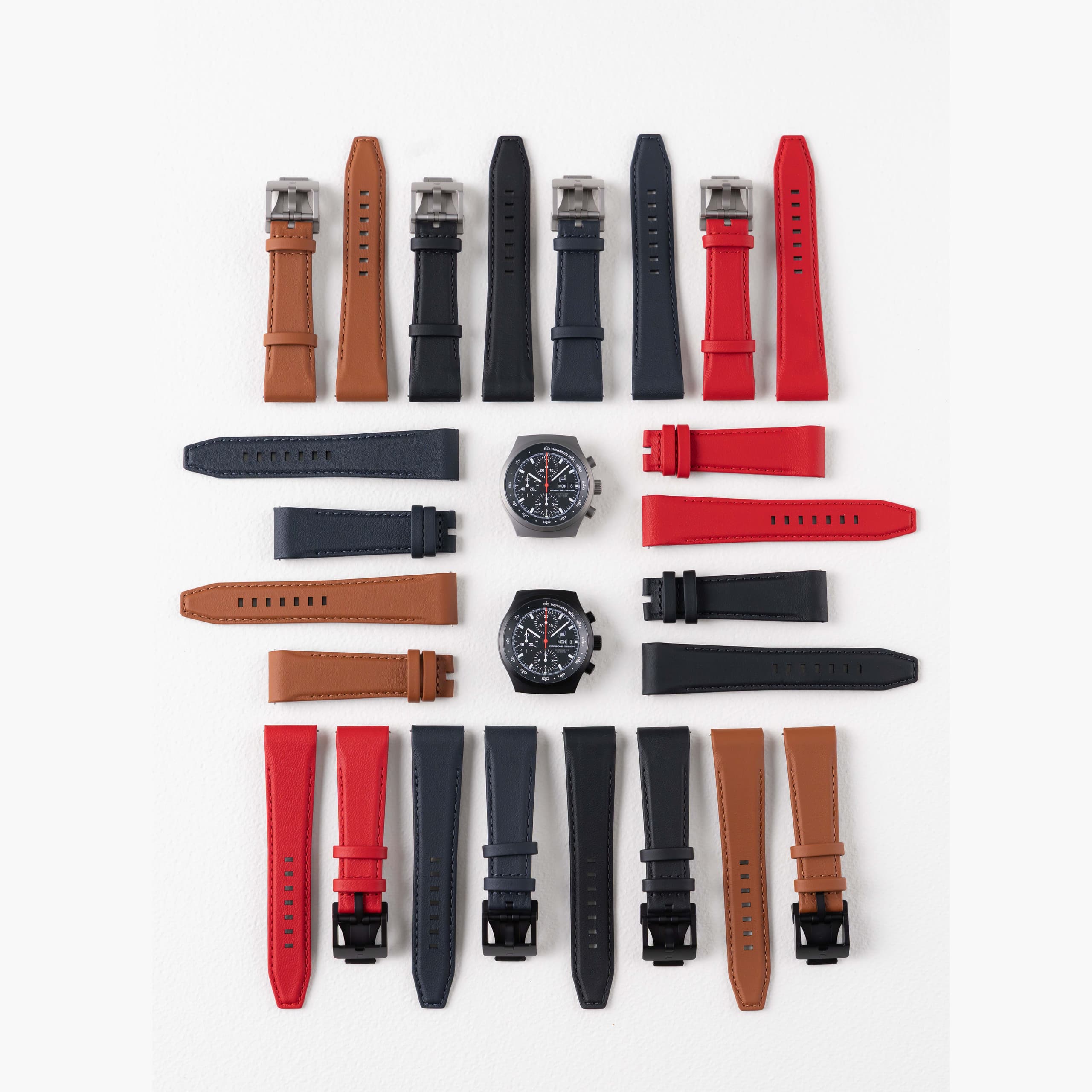 Varios correas de reloj de cuero con dos relojes cronógrafo sobre fondo blanco.