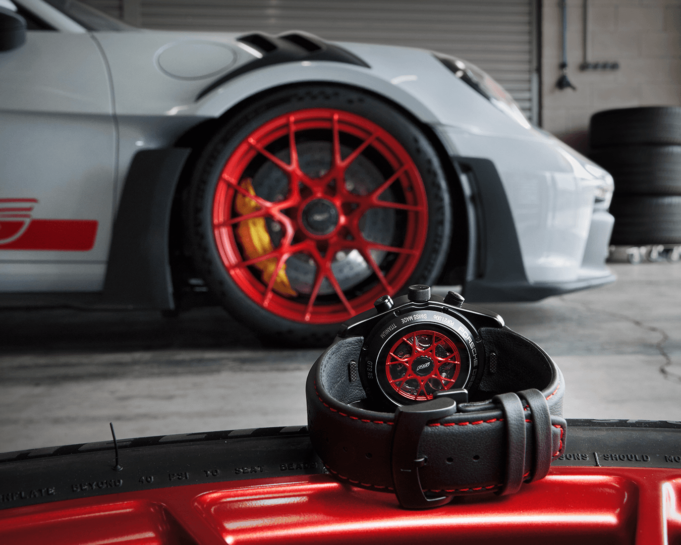 Zegarek Chronograph 1 GT3 RS widziany od tyłu; w tle biały Porsche 911 GT2 RS z czerwonymi detalami