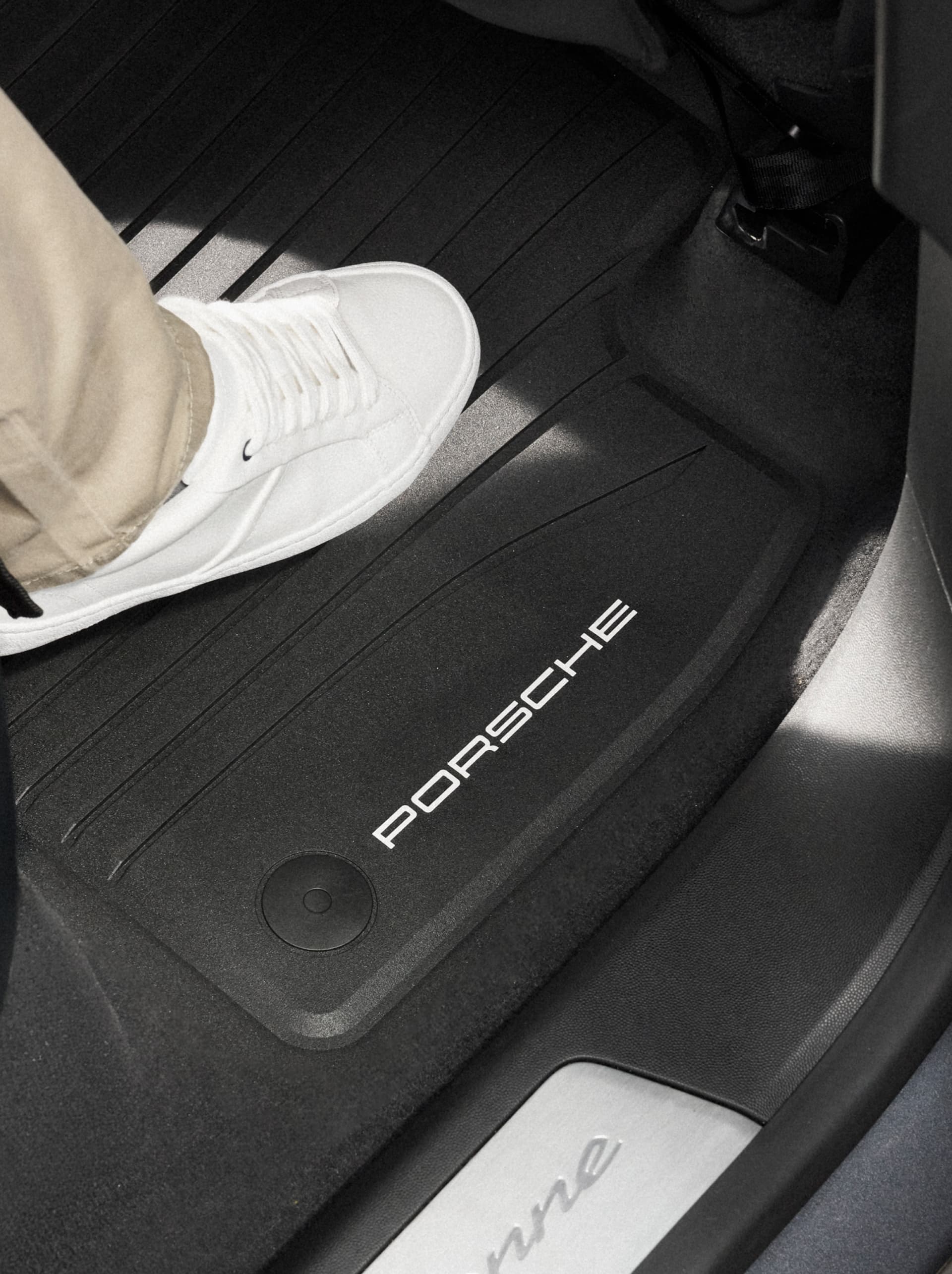 Sneaker bianca che calpesta un tappetino in gomma nero per tutte le stagioni Porsche con logo PORSCHE nel vano piedi dell’auto