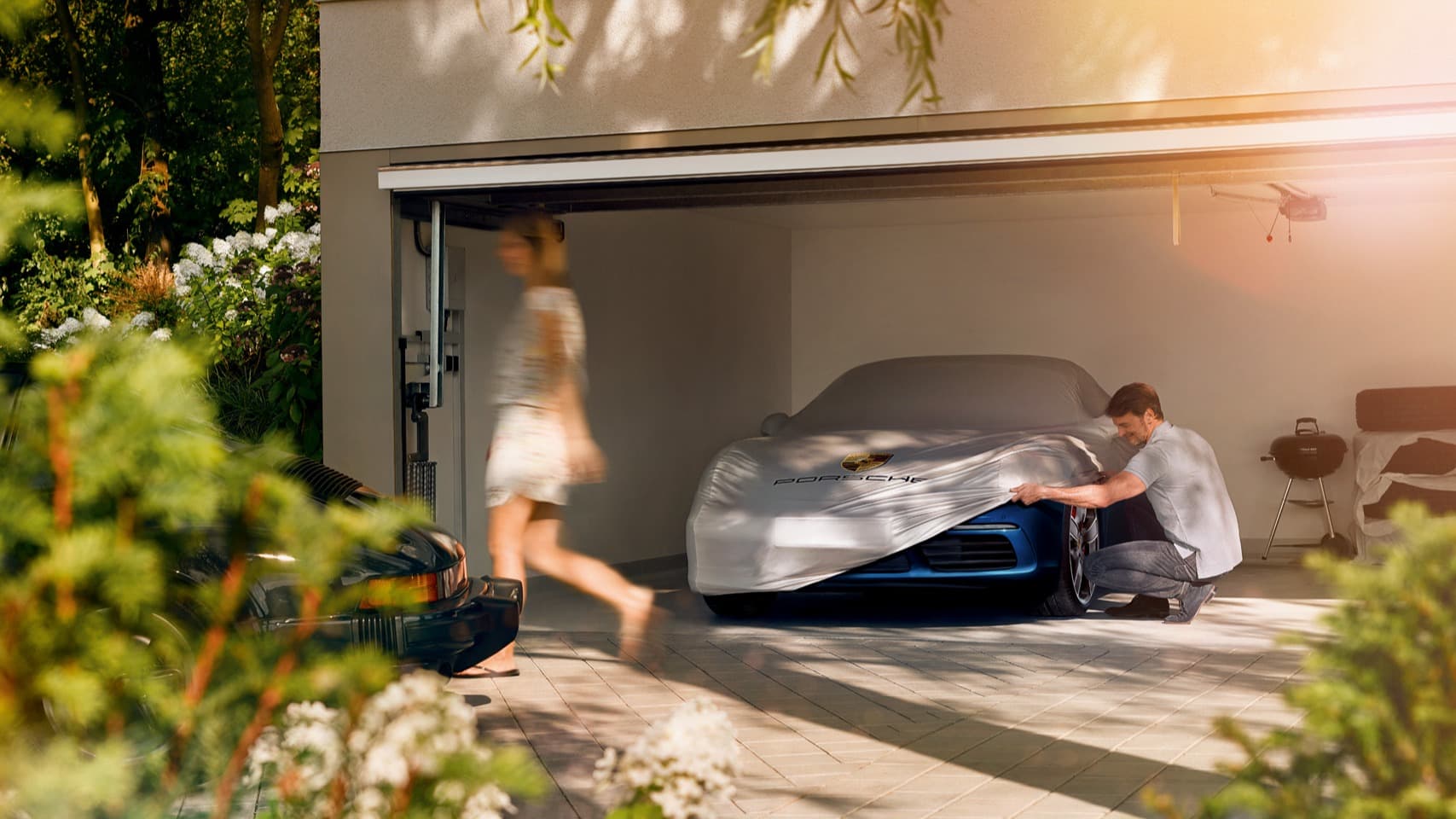You can see a man in a garage next to a Porsche car beneath a car cover