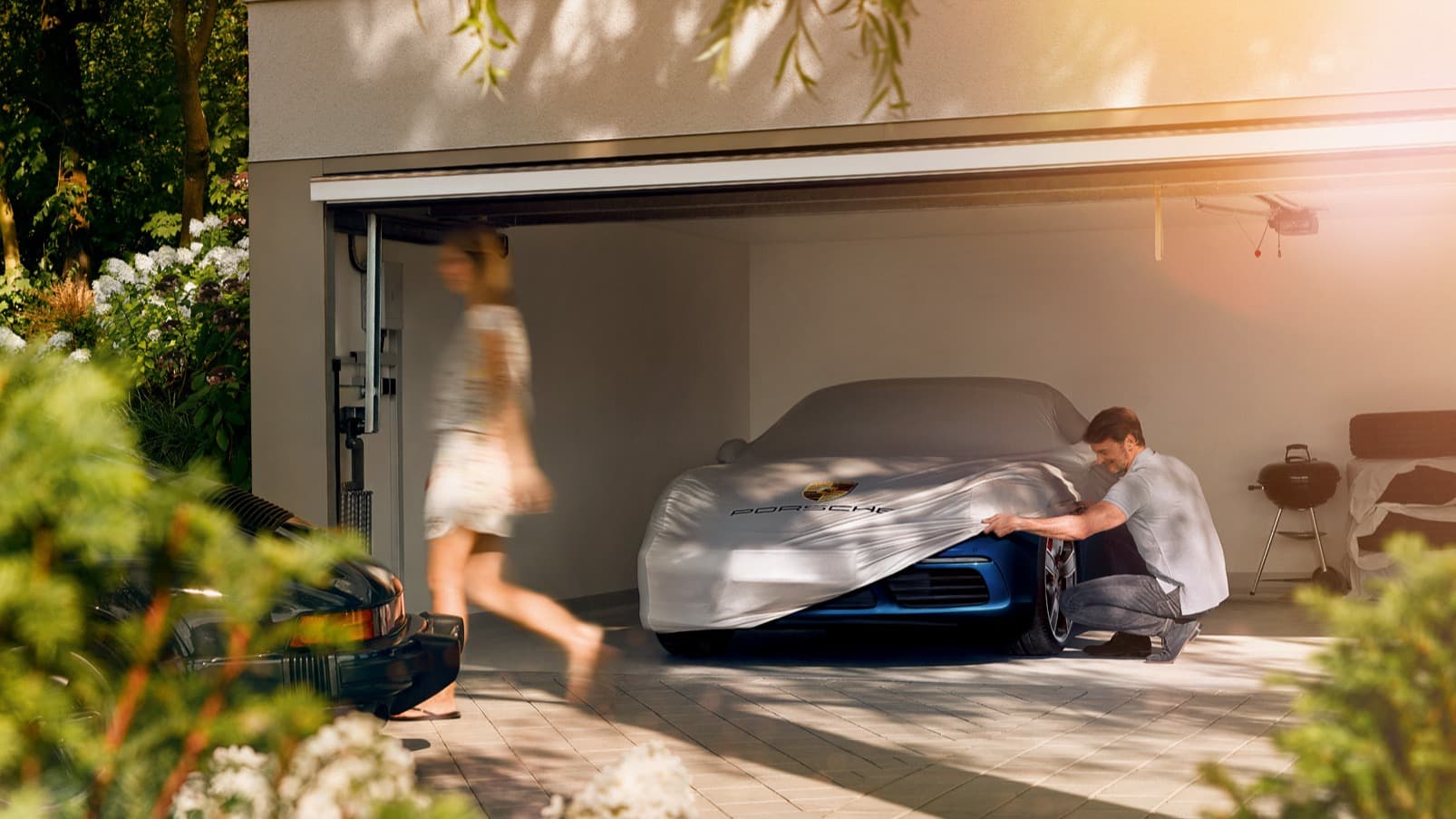 You can see a man in a garage next to a Porsche car beneath a car cover