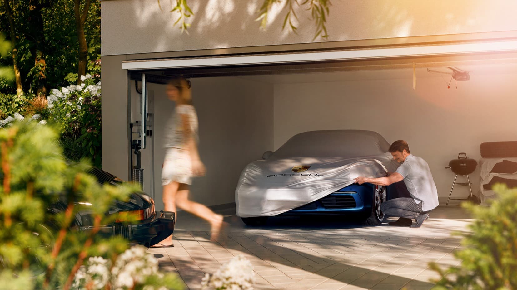 You can see a man in a garage next to a Porsche car beneath a car cover