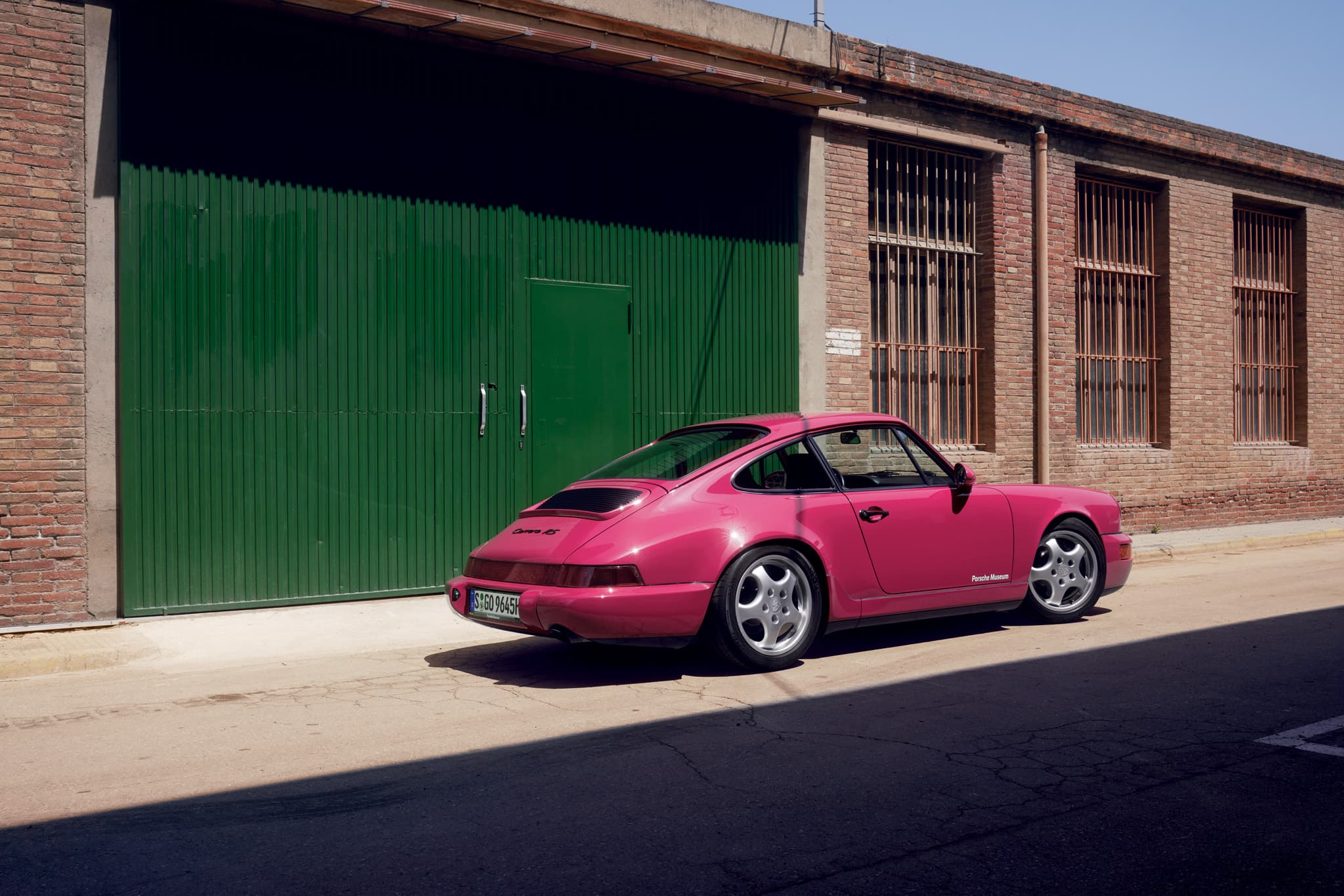 You can see a pink historic Porsche car in front of a garage with green doors