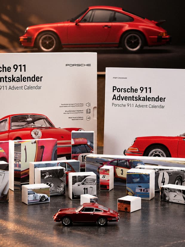 Set calendario dell’Avvento Porsche 911 con modelli 911 rossi, libro e piccole scatole su un tavolo, 911 rossa sullo sfondo