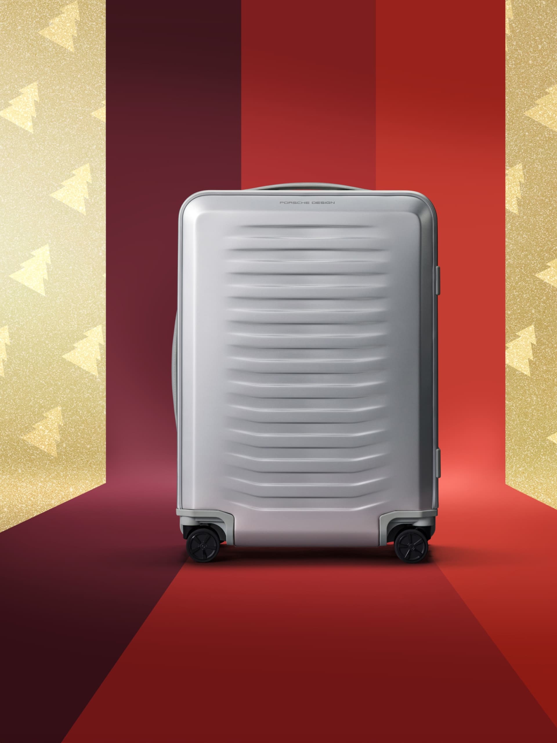 Silver suitcase with wheels on a red and gold festive background with tree patterns.