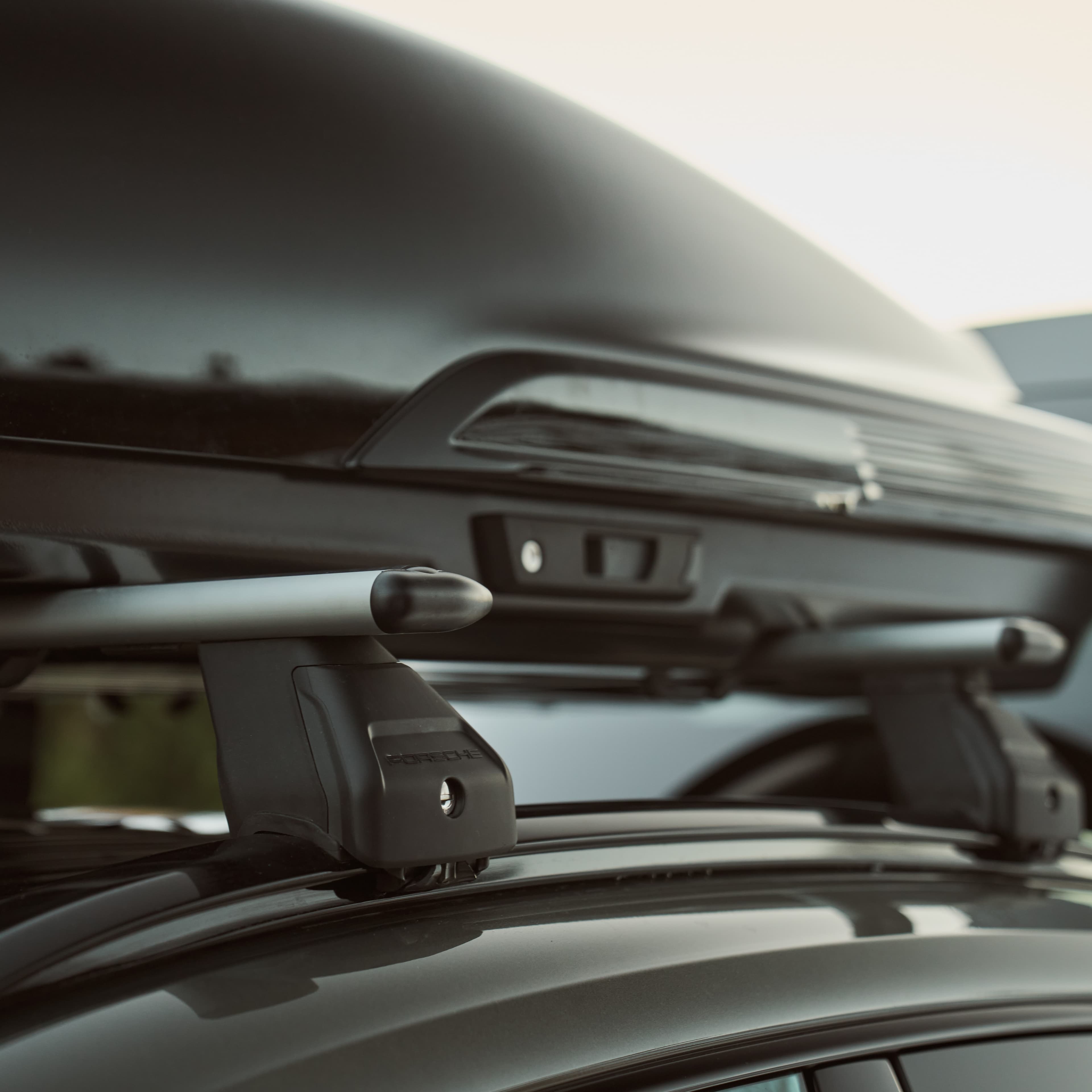 Car roof with black cargo box and silver crossbars, close-up view, highlighting sleek design and attachment details.