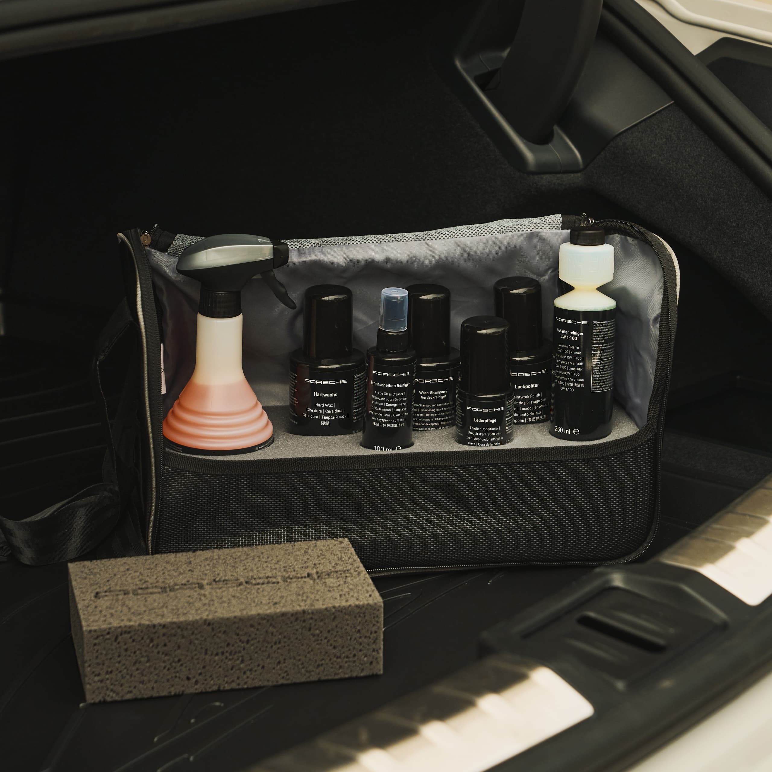 Kfz-Pflegeset im Kofferraum mit Sprühflasche, Reinigungsprodukten und Schwamm, ordentlich in einer schwarzen Tasche organisiert.