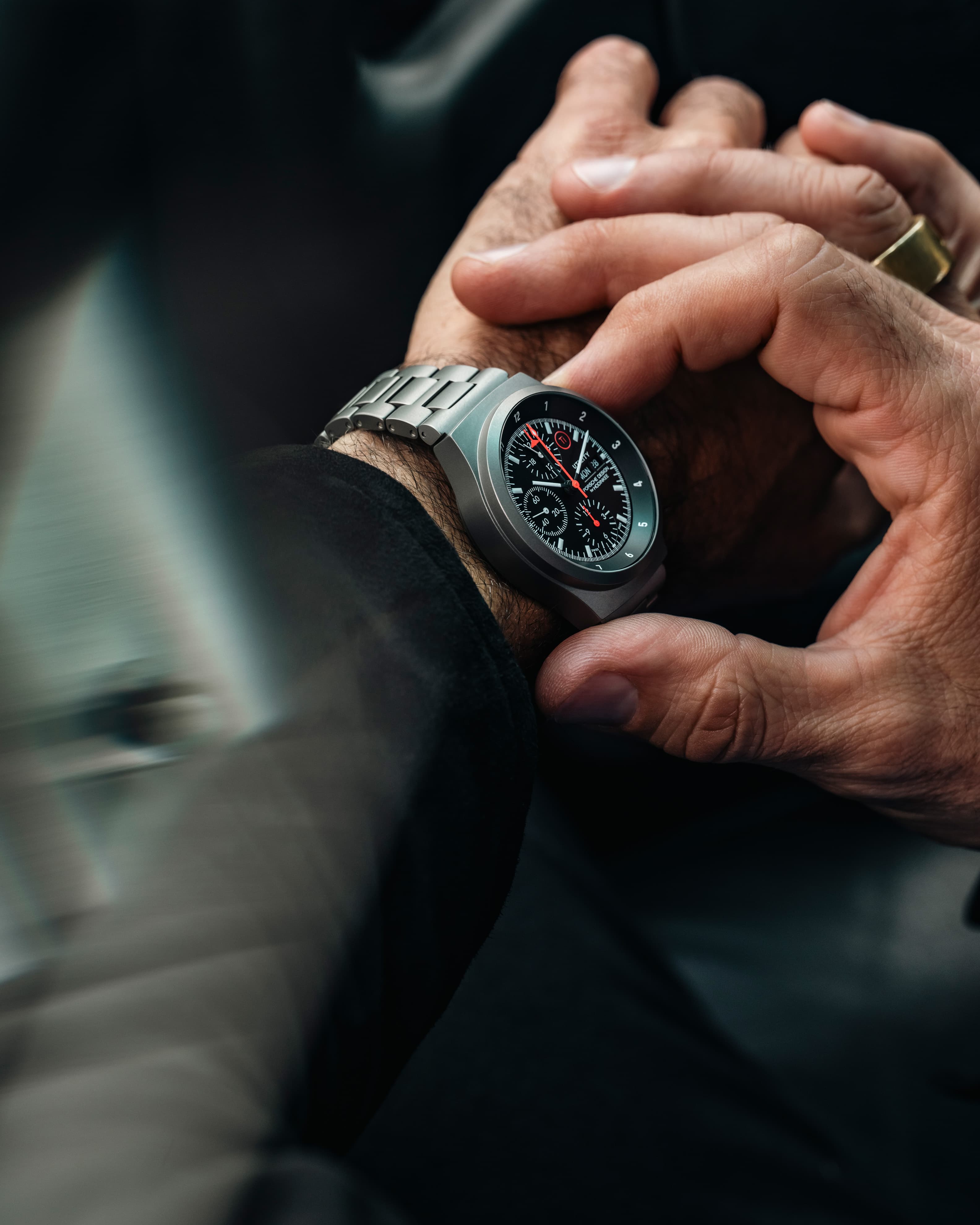 Mano che regola un orologio da polso cronografo in metallo argentato con quadrante nero e lancette rosse, primo piano nell’abitacolo dell’auto