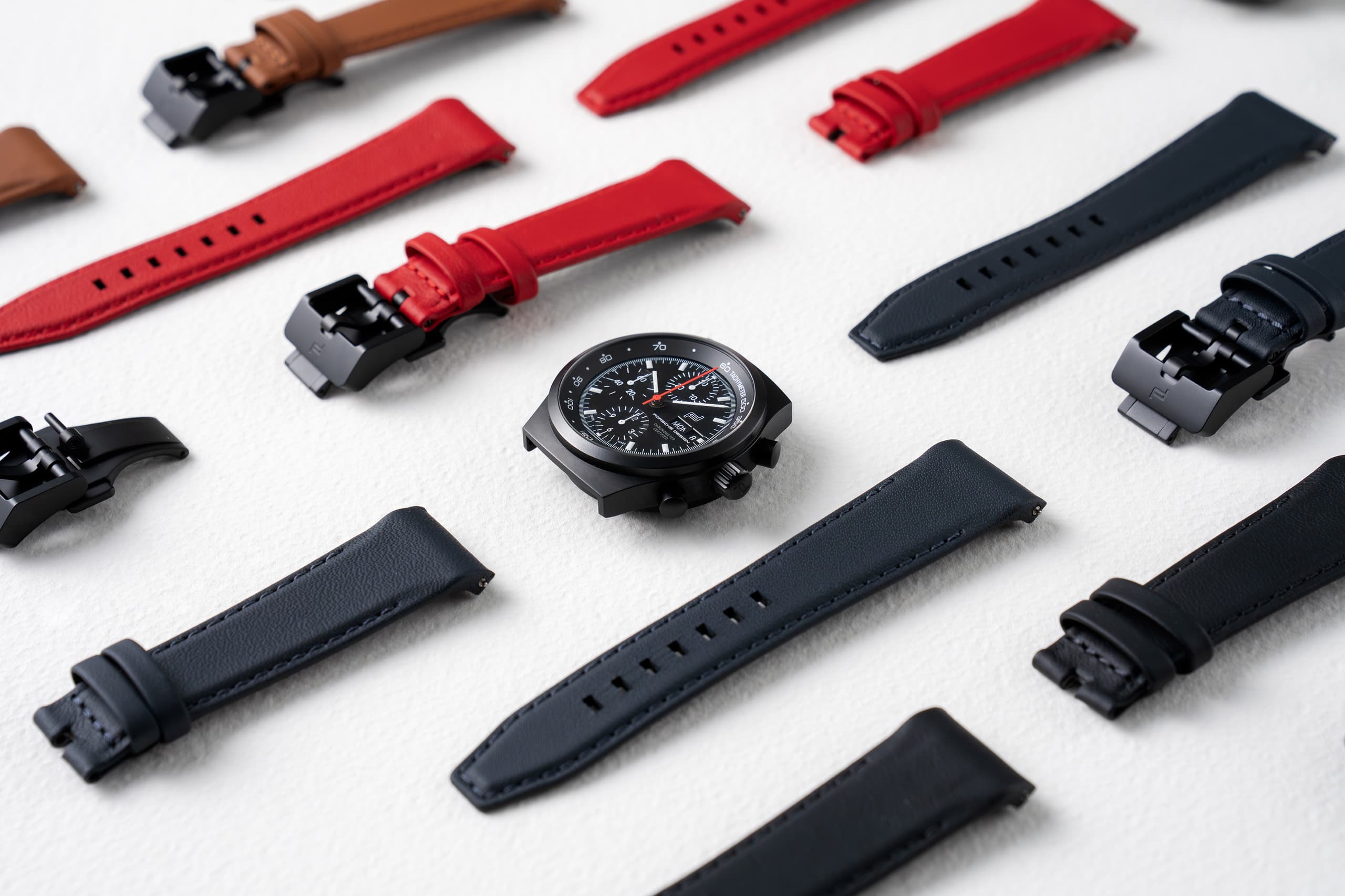 Black chronograph watch with interchangeable red, black and brown leather straps on a light background