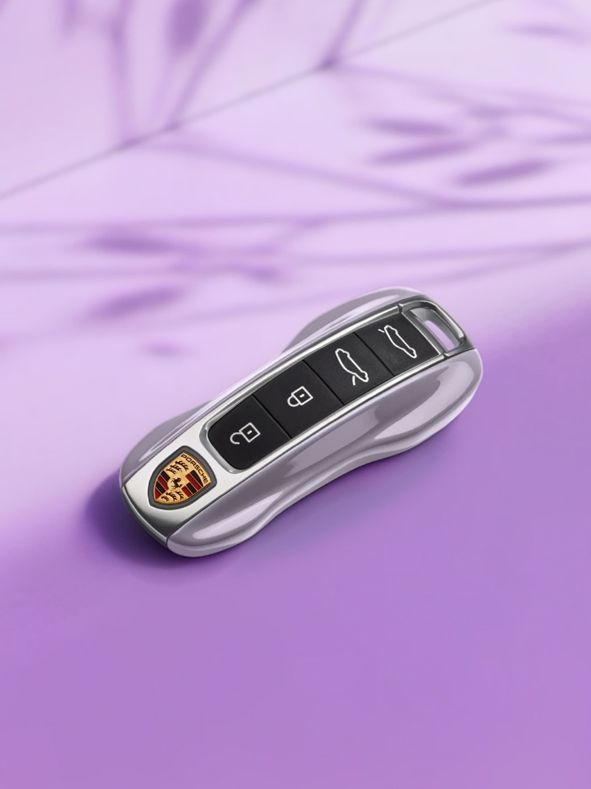 Llave de coche Porsche plateada con botones negros sobre fondo morado.