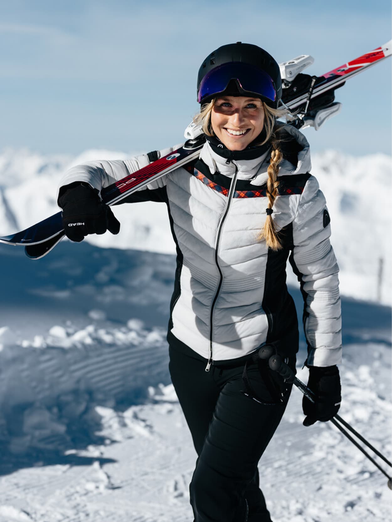 Woman in the snowy mountains wearing ski clothing and ski on her shoulder