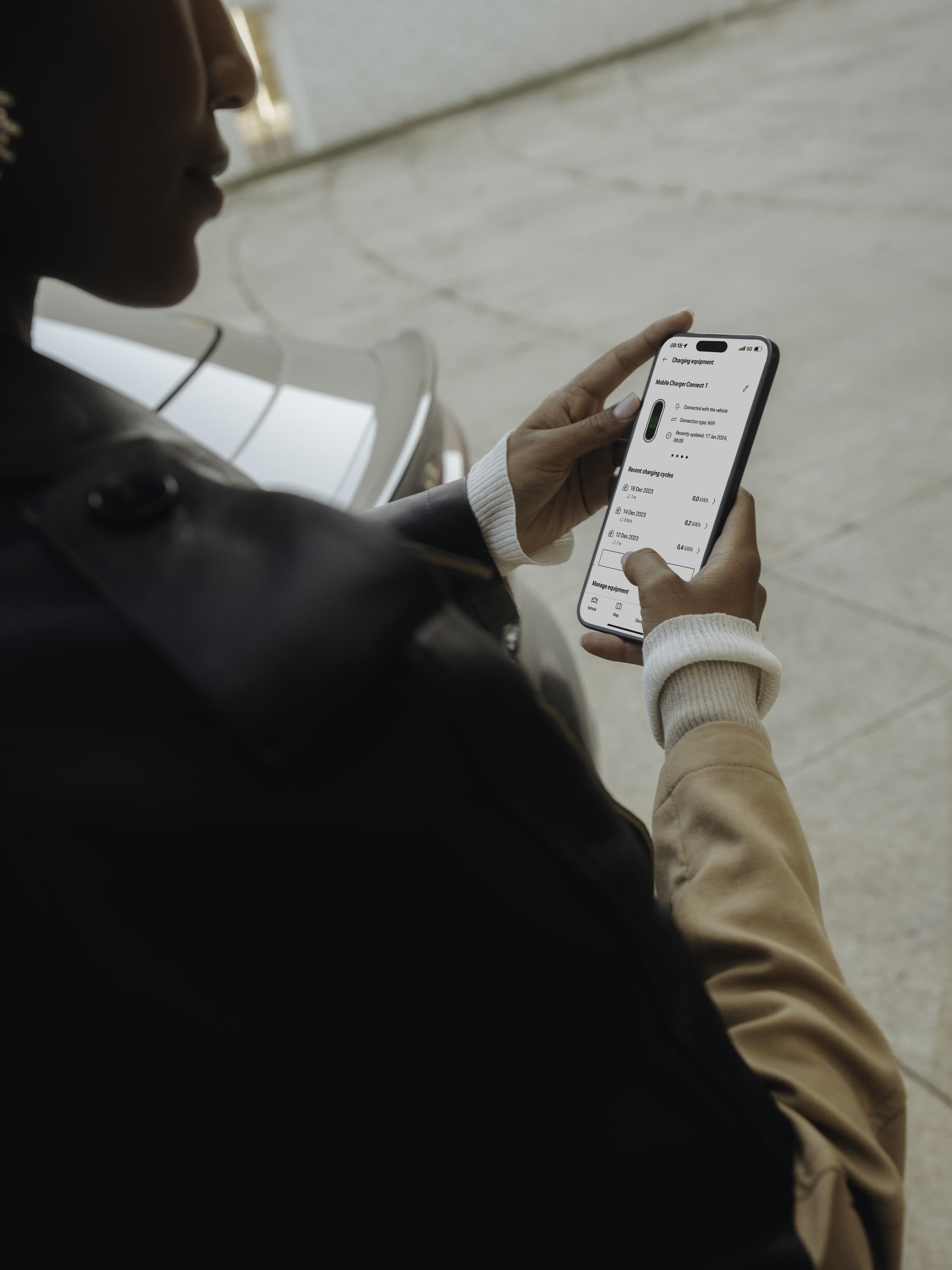 Personne en veste utilisant une application smartphone près d'une voiture garée, affichant les détails de charge à l'écran.